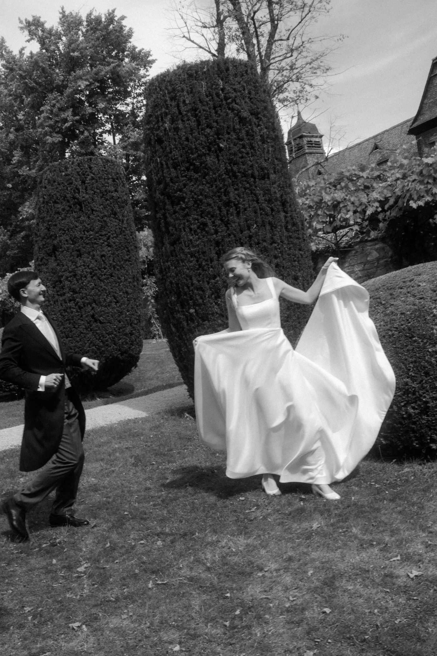 Black and white wedding photos captured in a garden with topiary bushes.