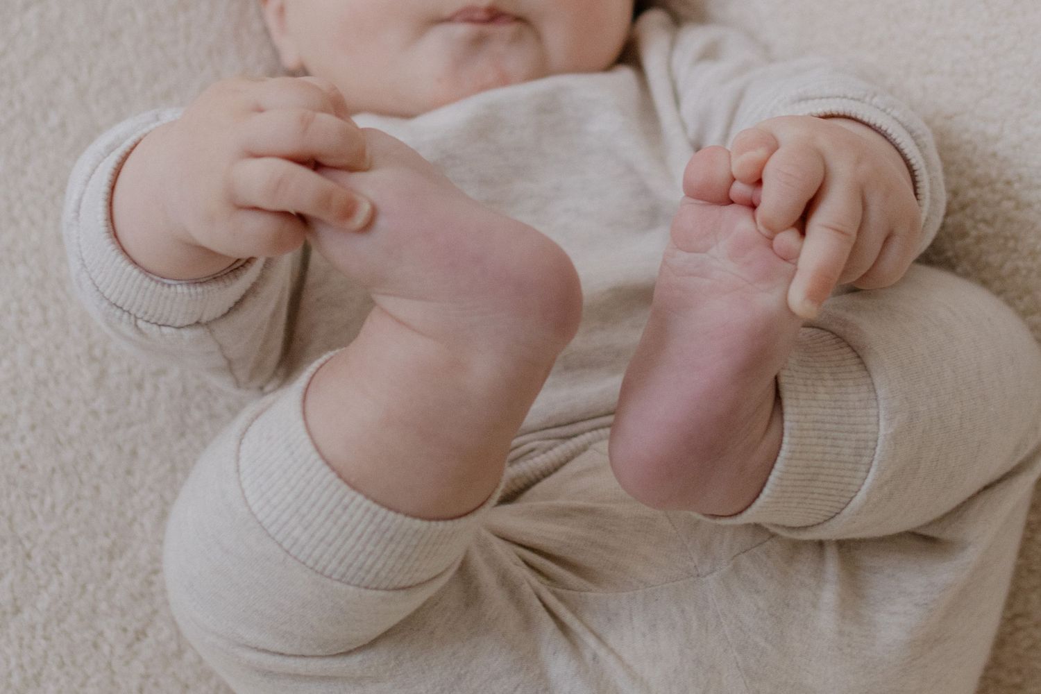 Close-up details of a baby's feet and hands in soft natural lighting.