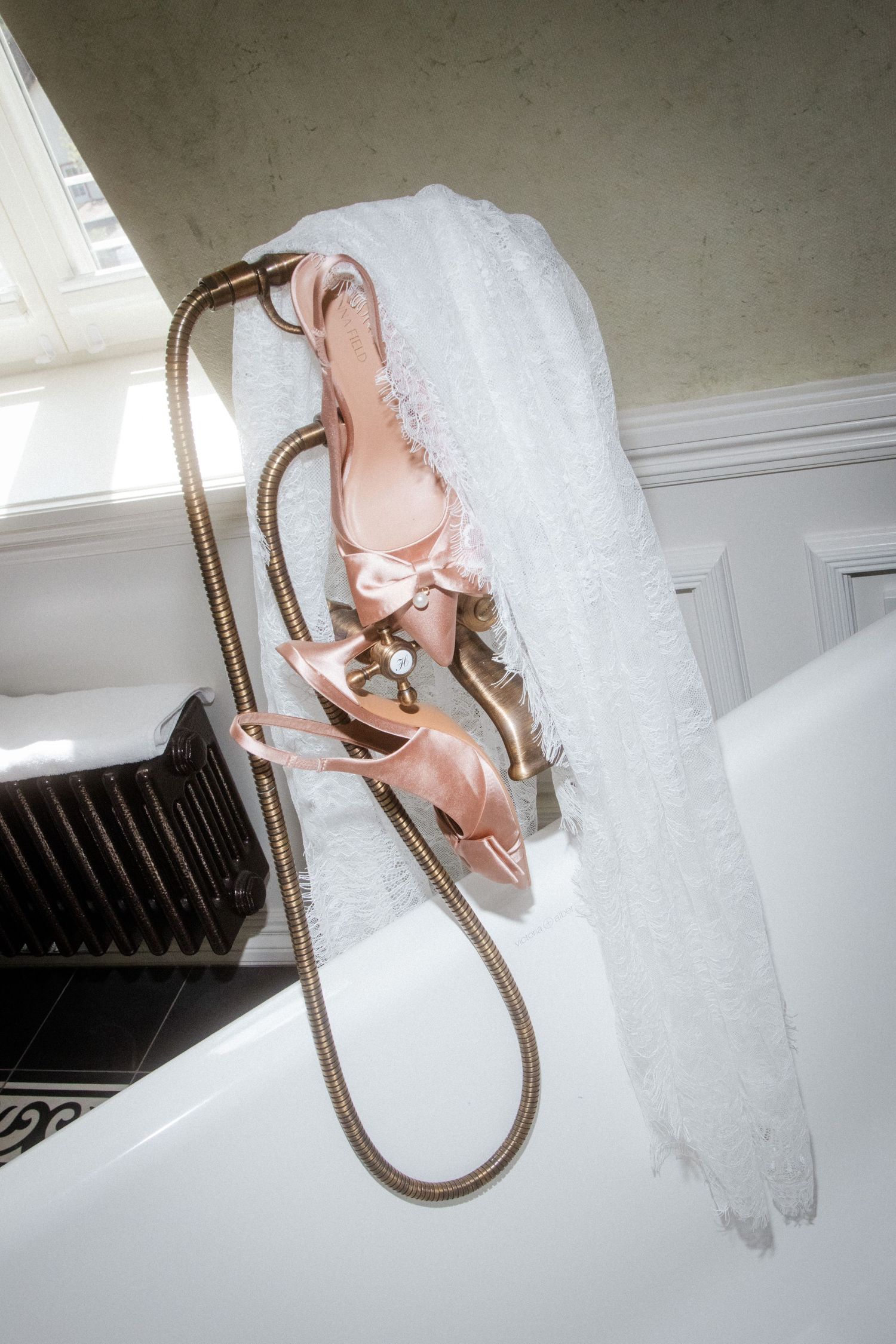 Pink bridal heels and white wedding veil draped over a vintage bathtub faucet in an elegant bathroom.