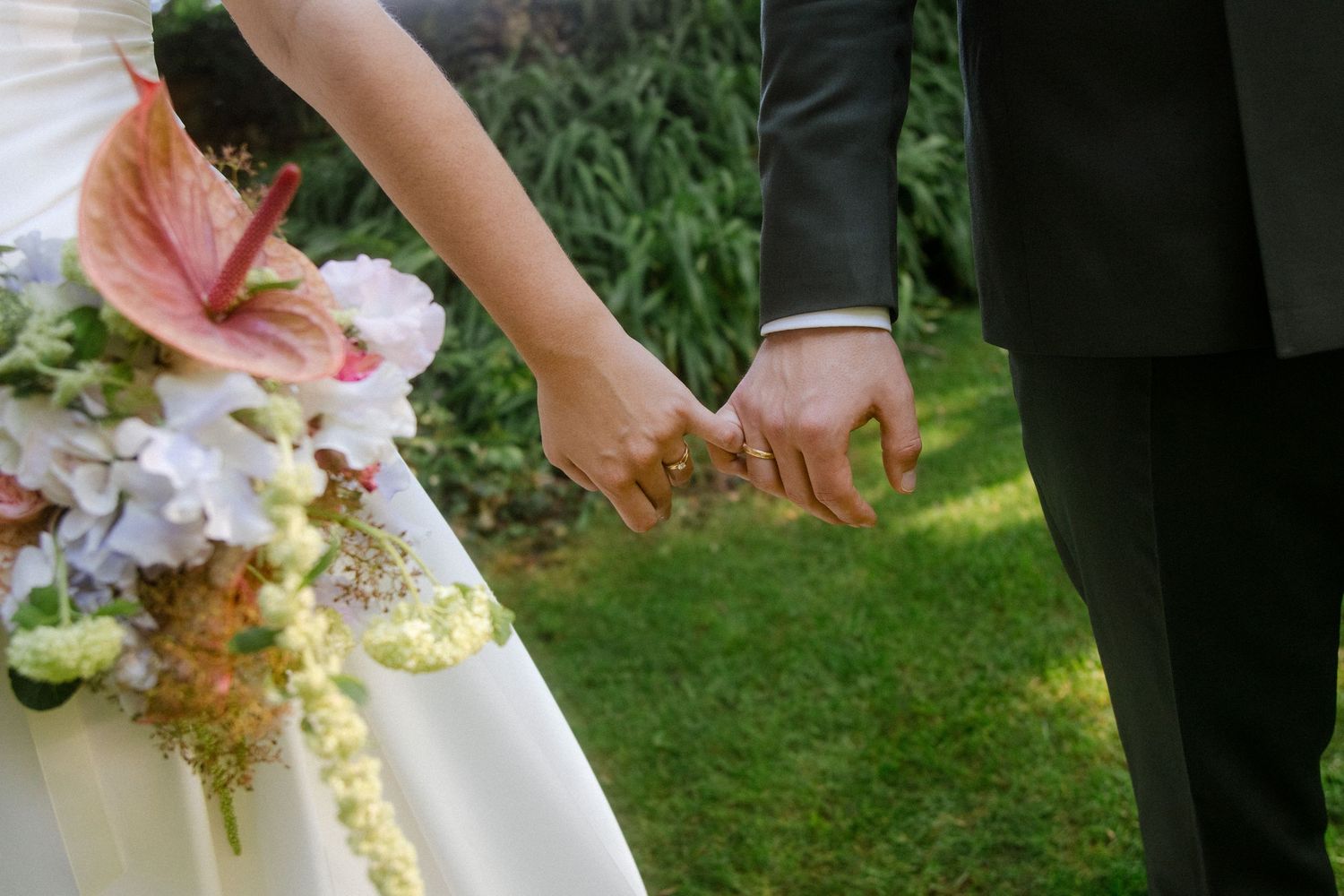 Hands holding delicate floral arrangements against white wedding dress fabric.