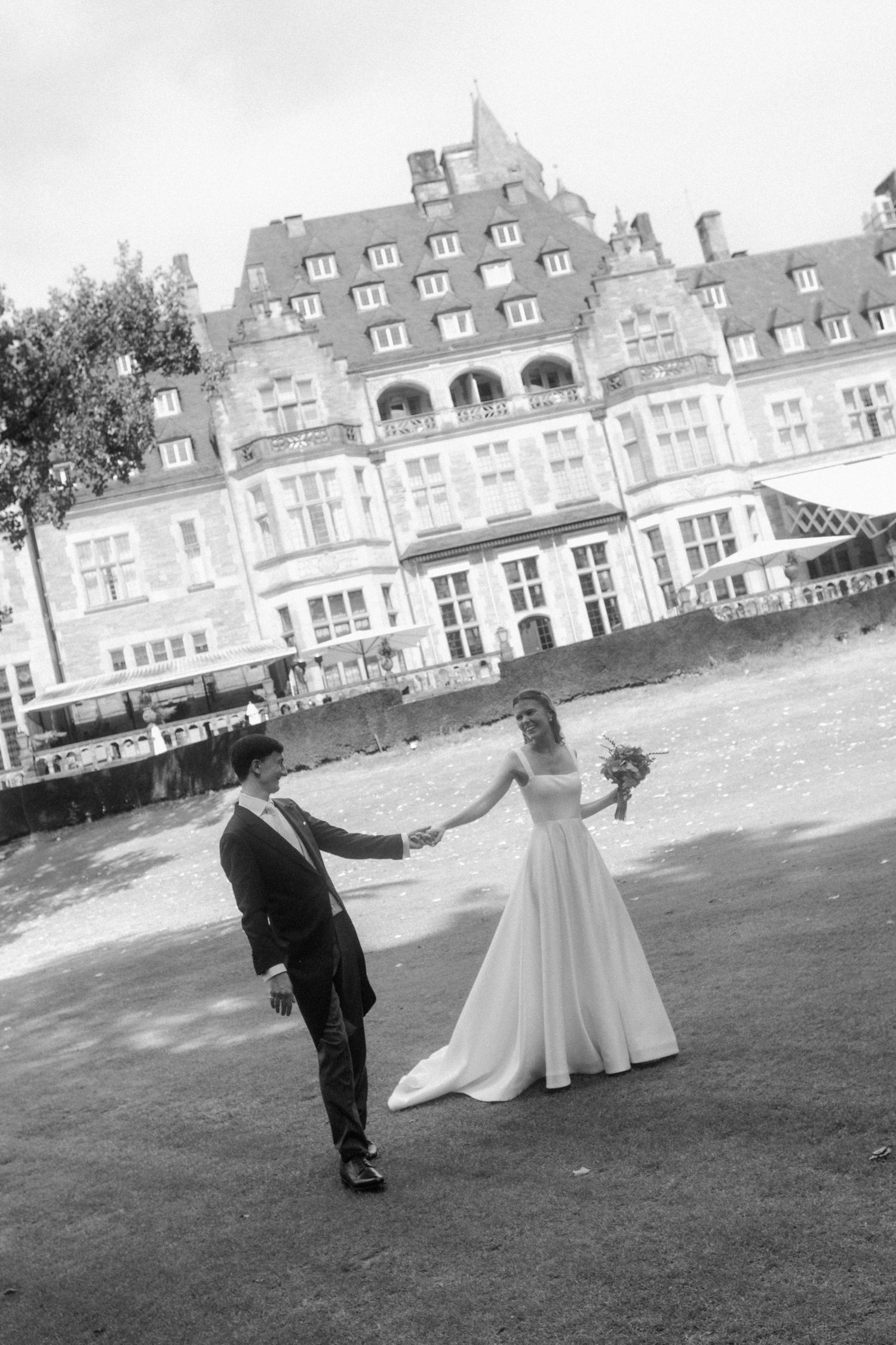 Black and white wedding photo with couple on lawn in front of stately mansion.