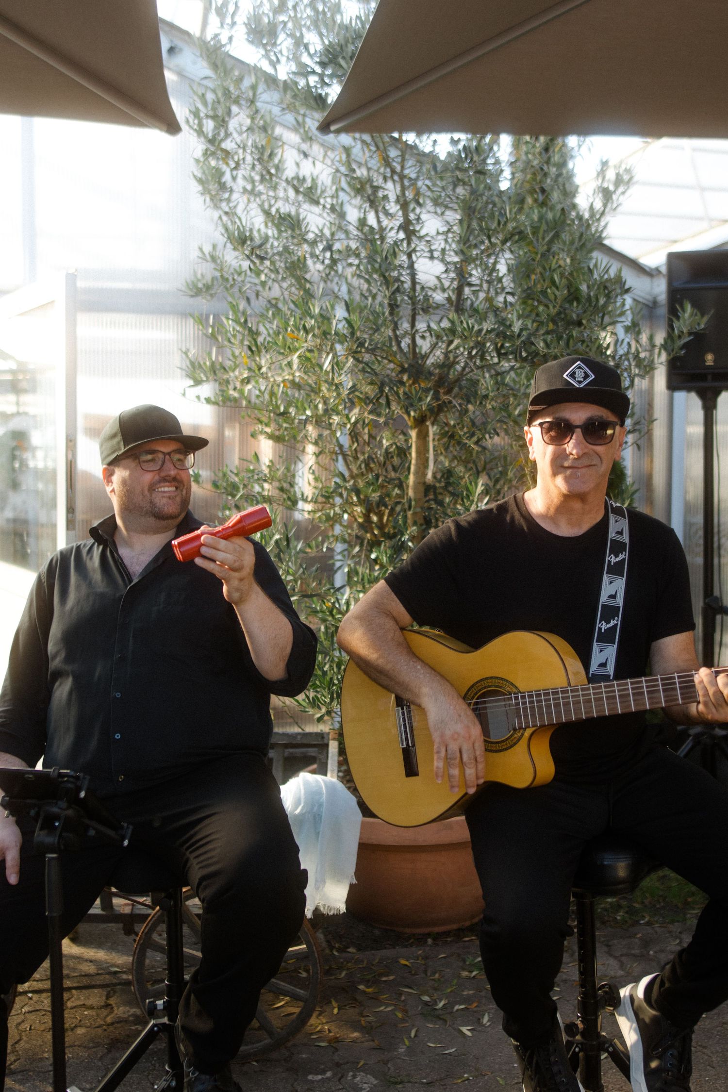 Musicians performing outdoors with acoustic guitar under patio umbrellas.