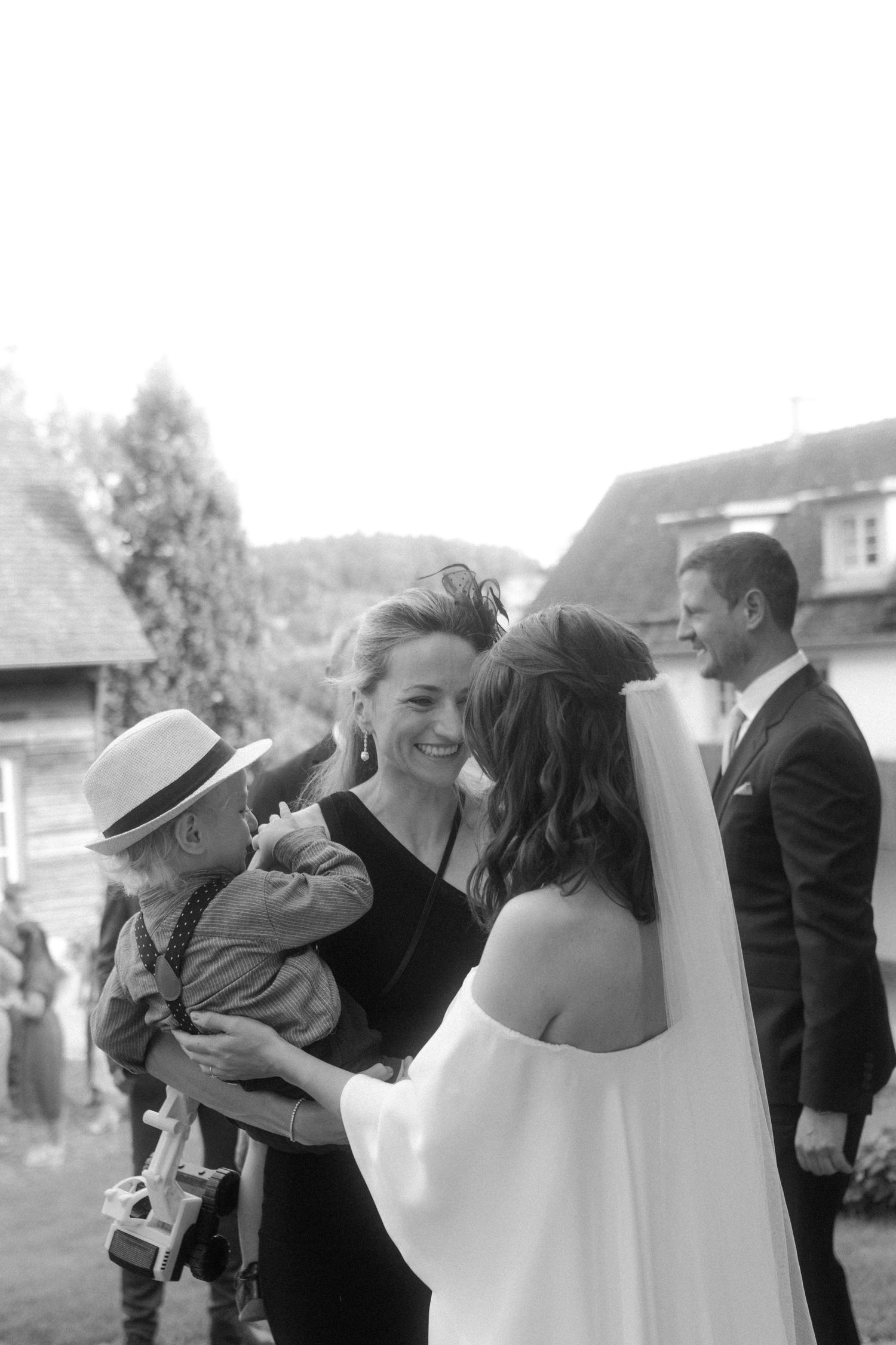 Black and white candid photo of wedding guests sharing emotional moments outdoors.