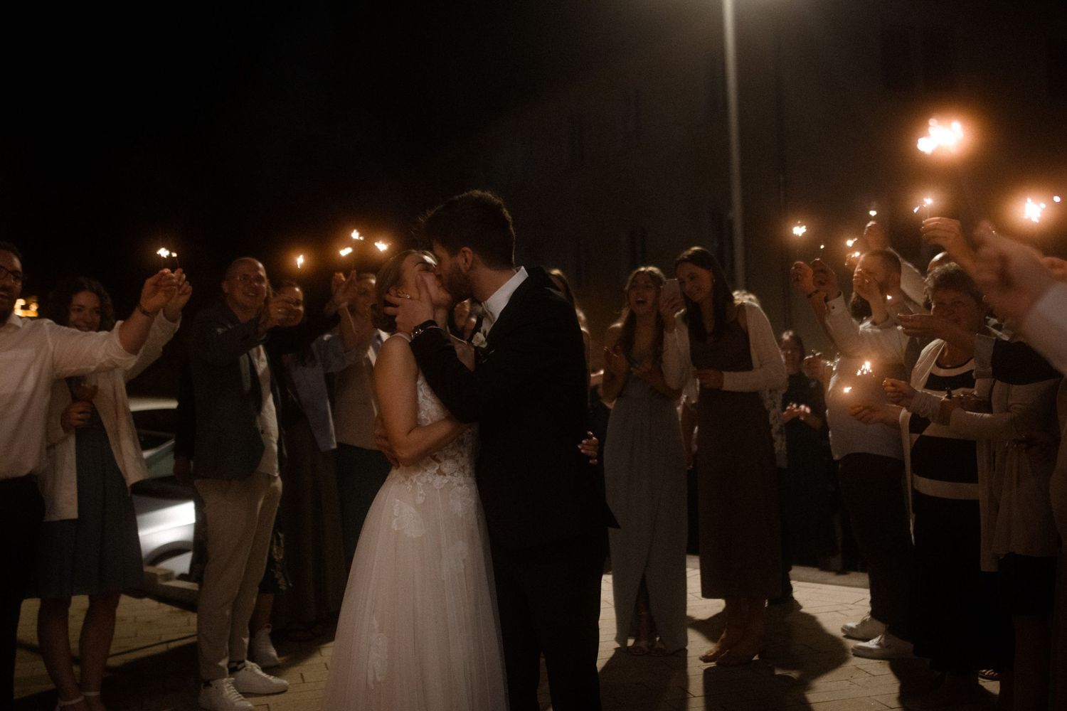 A wedding couple shares an intimate moment outdoors surrounded by candlelight and guests.