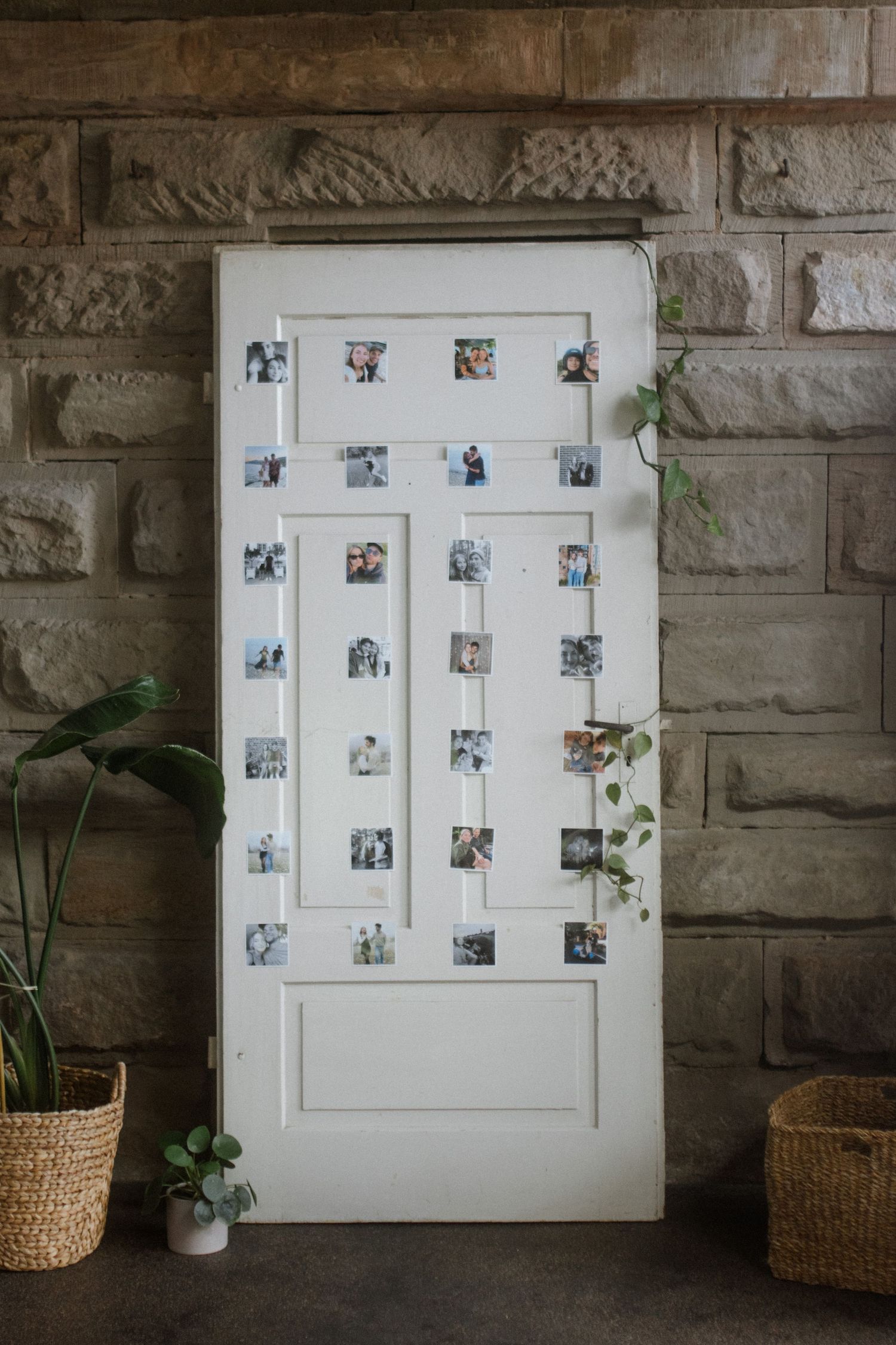 White door decorated with small polaroid photos arranged in vertical lines against stone wall.