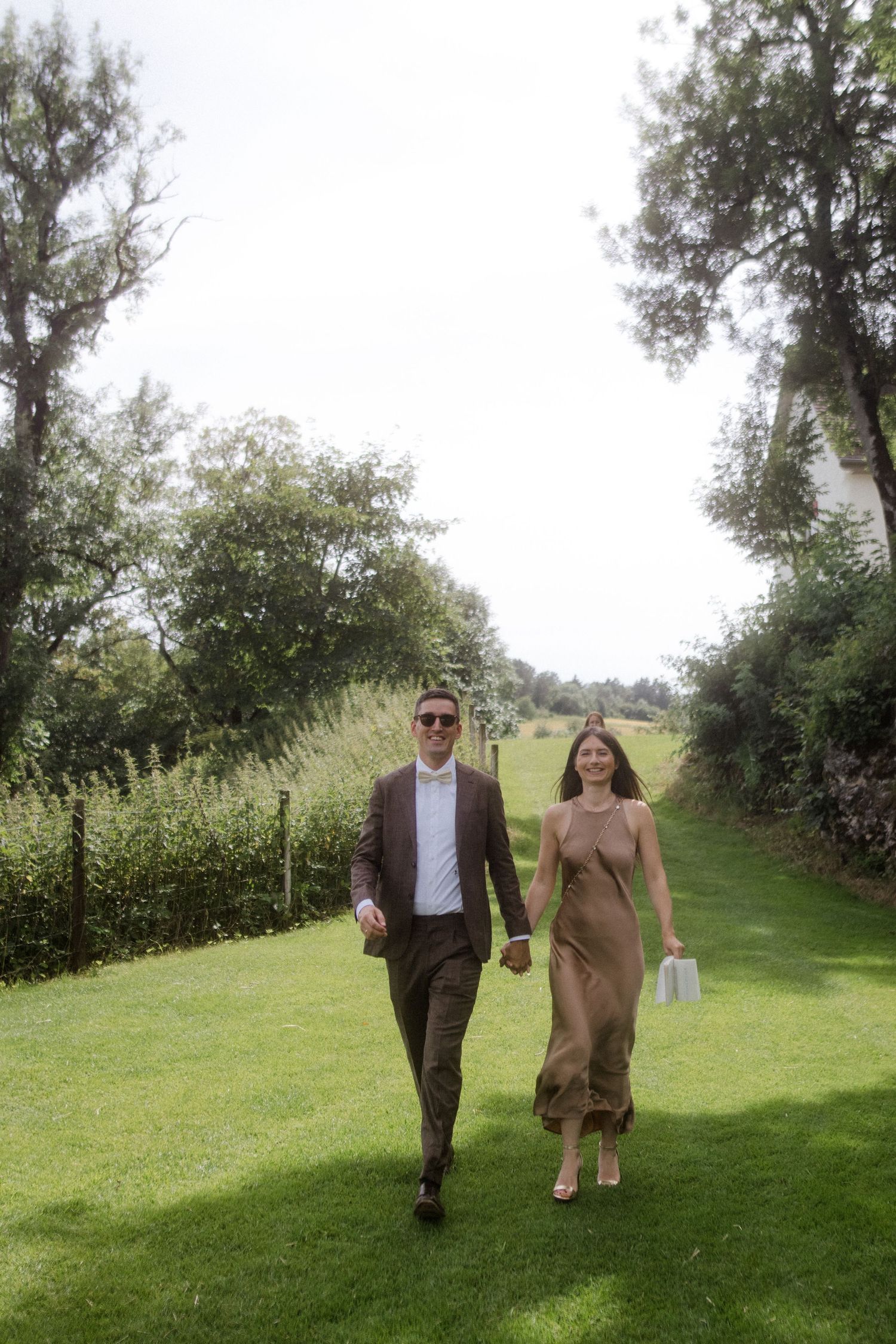 A couple walks together on a manicured lawn path between green hedges.