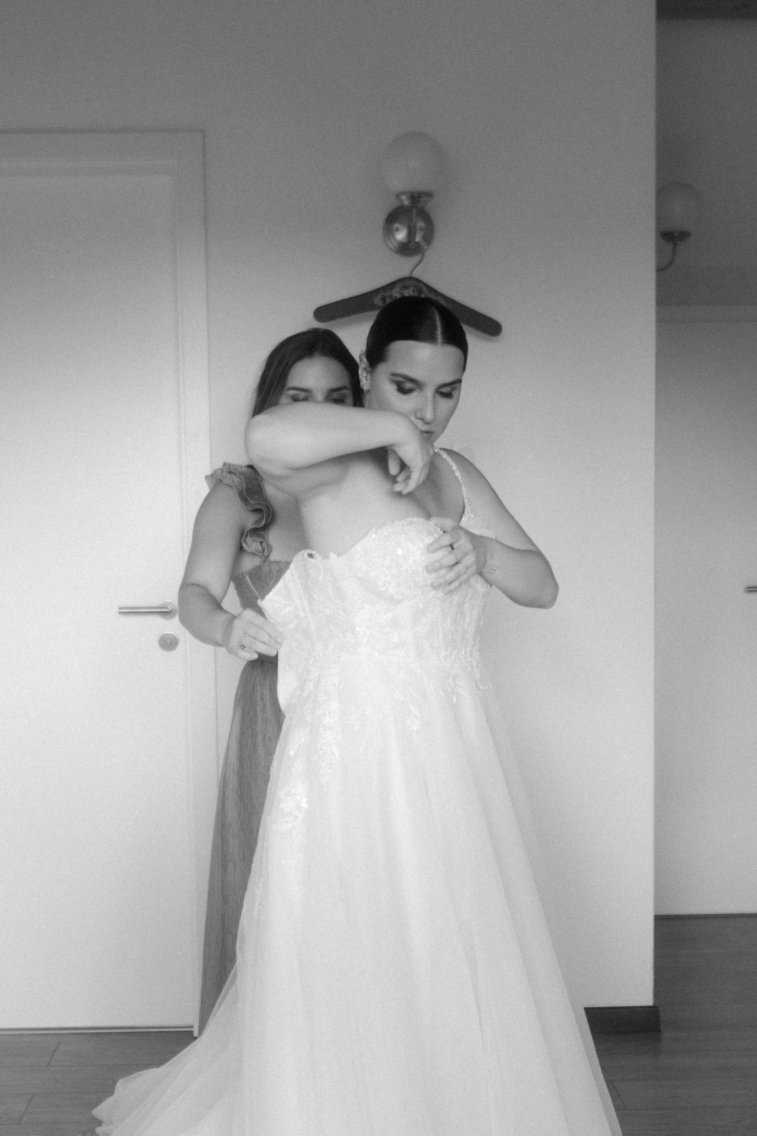 Black and white image of wedding dress preparation with helping hands.