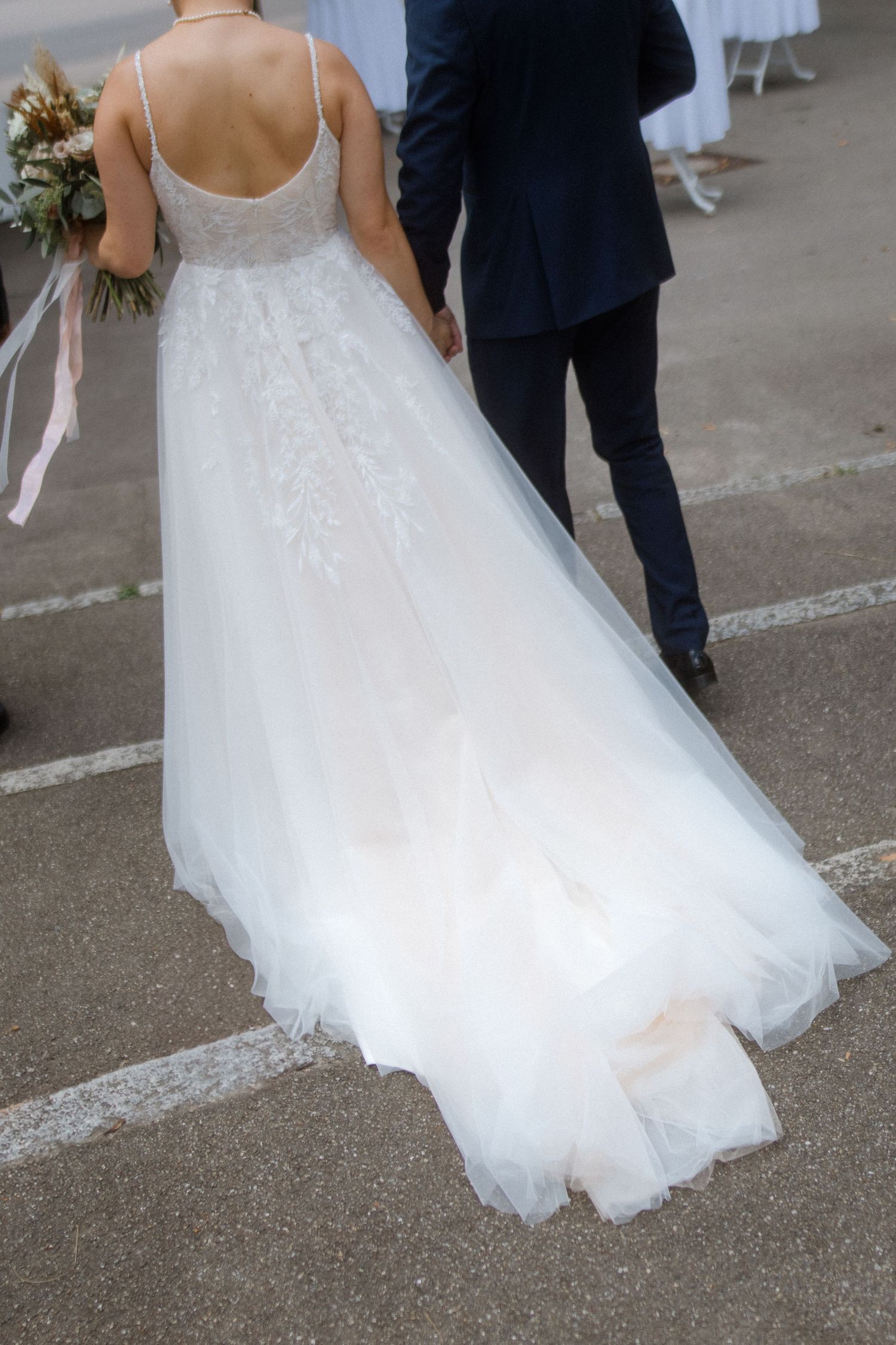 Back view of flowing white wedding dress train on concrete path.
