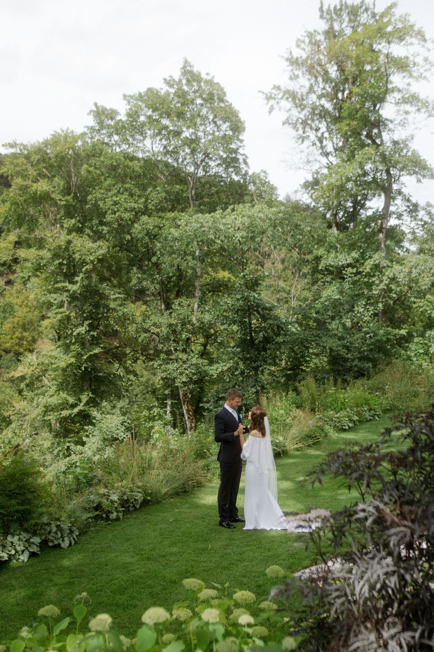 A wide shot of newlyweds embracing in a lush garden landscape.