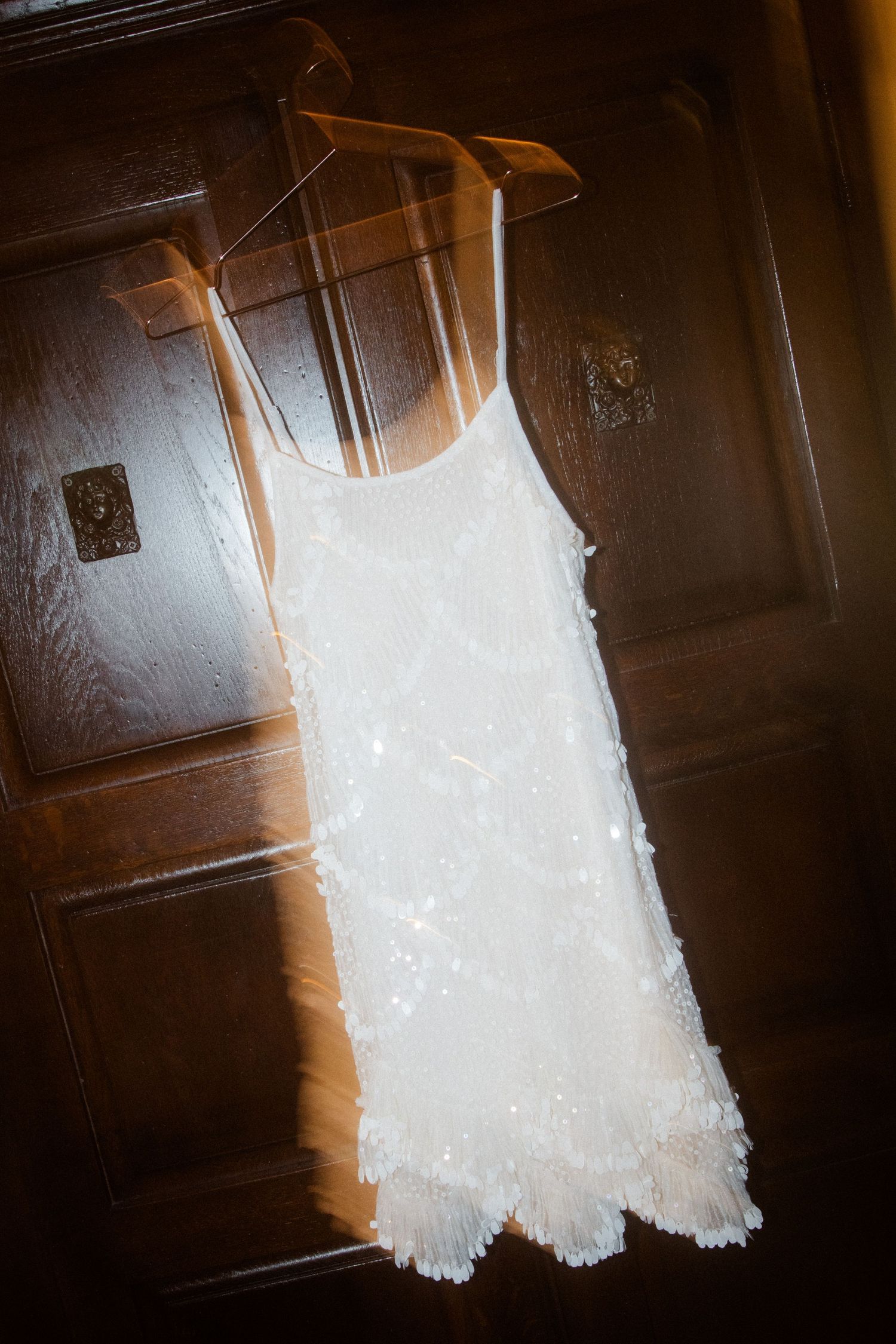 A delicate white lace dress hangs against a dark wooden door.