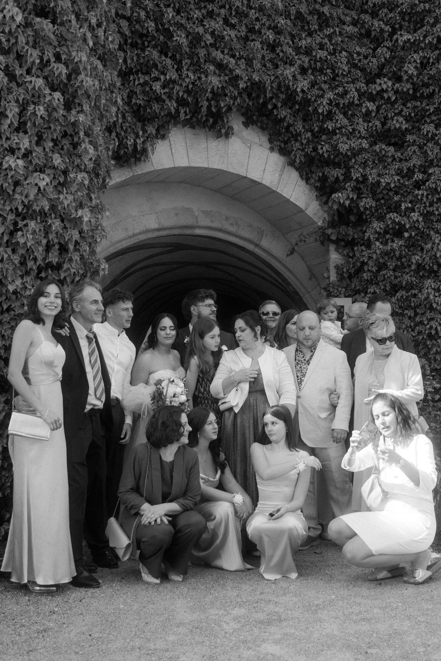Wedding party poses casually against ivy-covered wall for group photos.