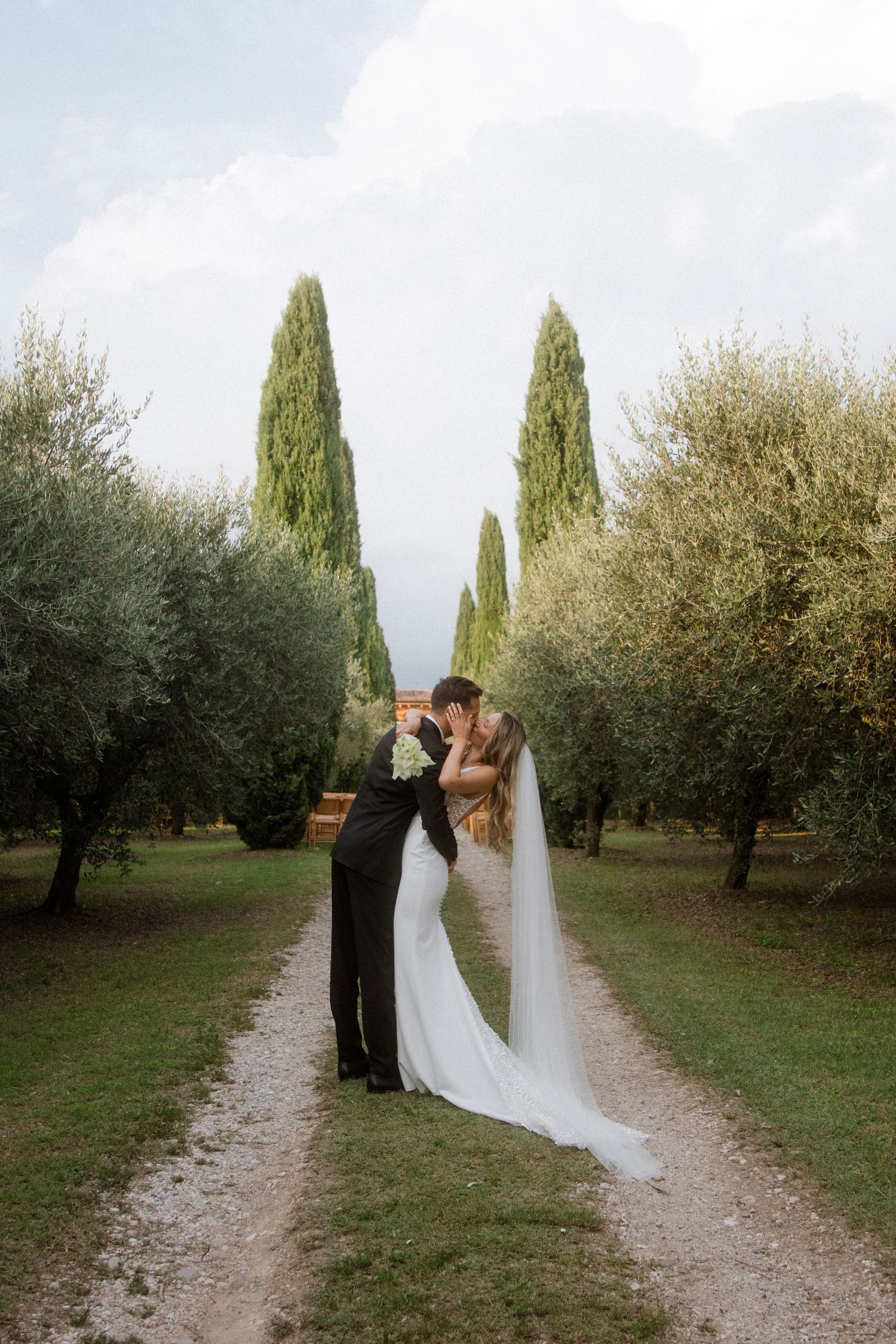 Romantic wedding portrait on a garden path surrounded by olive trees and cypress.