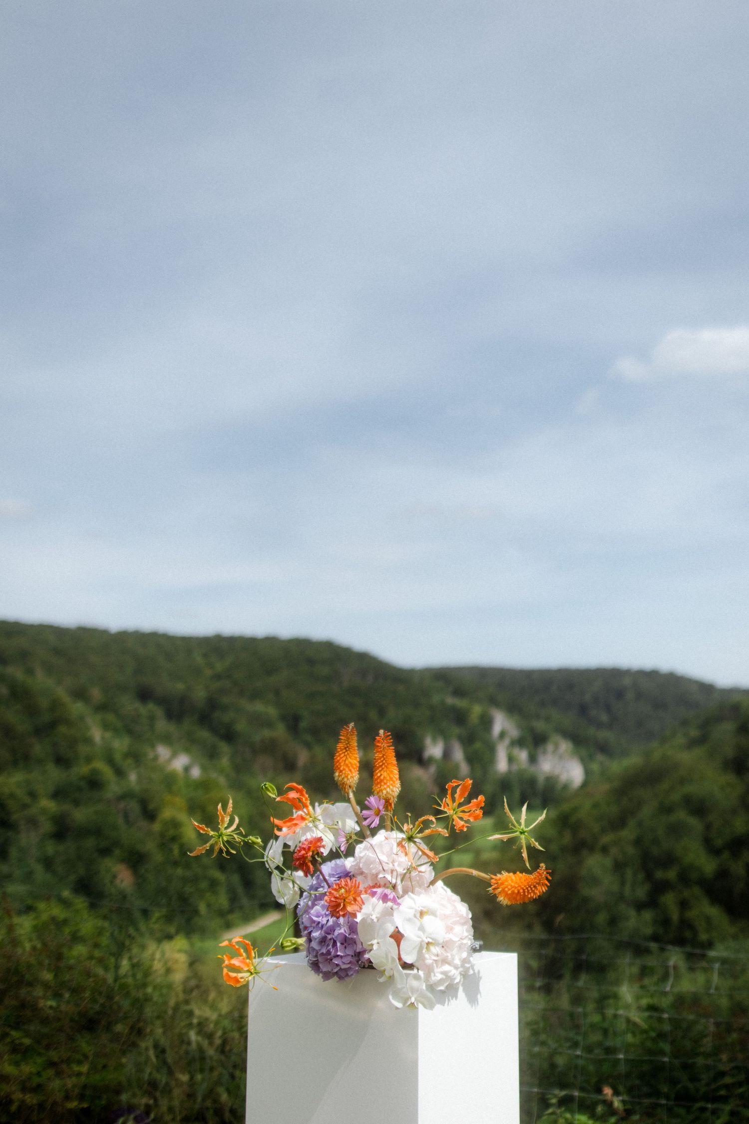 Elegant floral arrangement with orange and white flowers against a mountain backdrop.