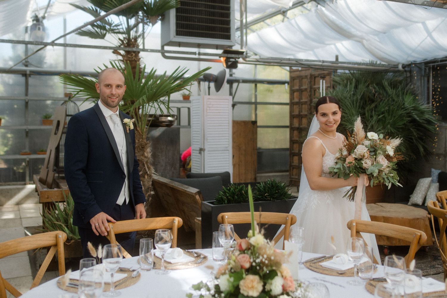 A wedding reception setup in a greenhouse with elegant table settings and natural lighting.
