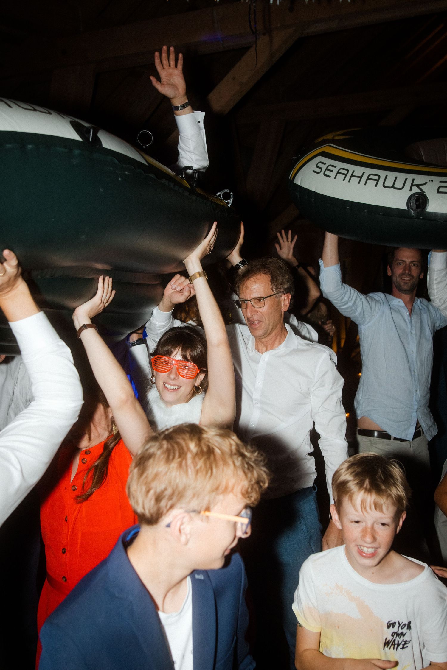 Crowd of excited party guests raising hands and cheering under decorative lighting.