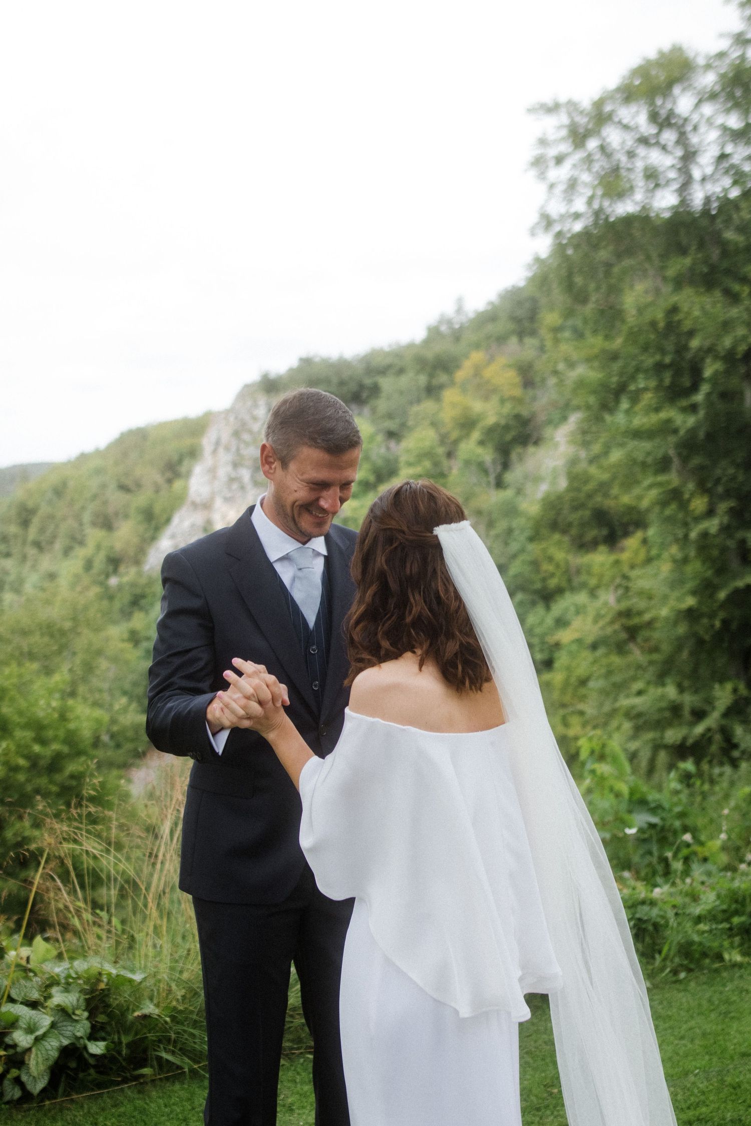 Newlyweds share a joyful moment while dancing in a garden with cliffs in the background.