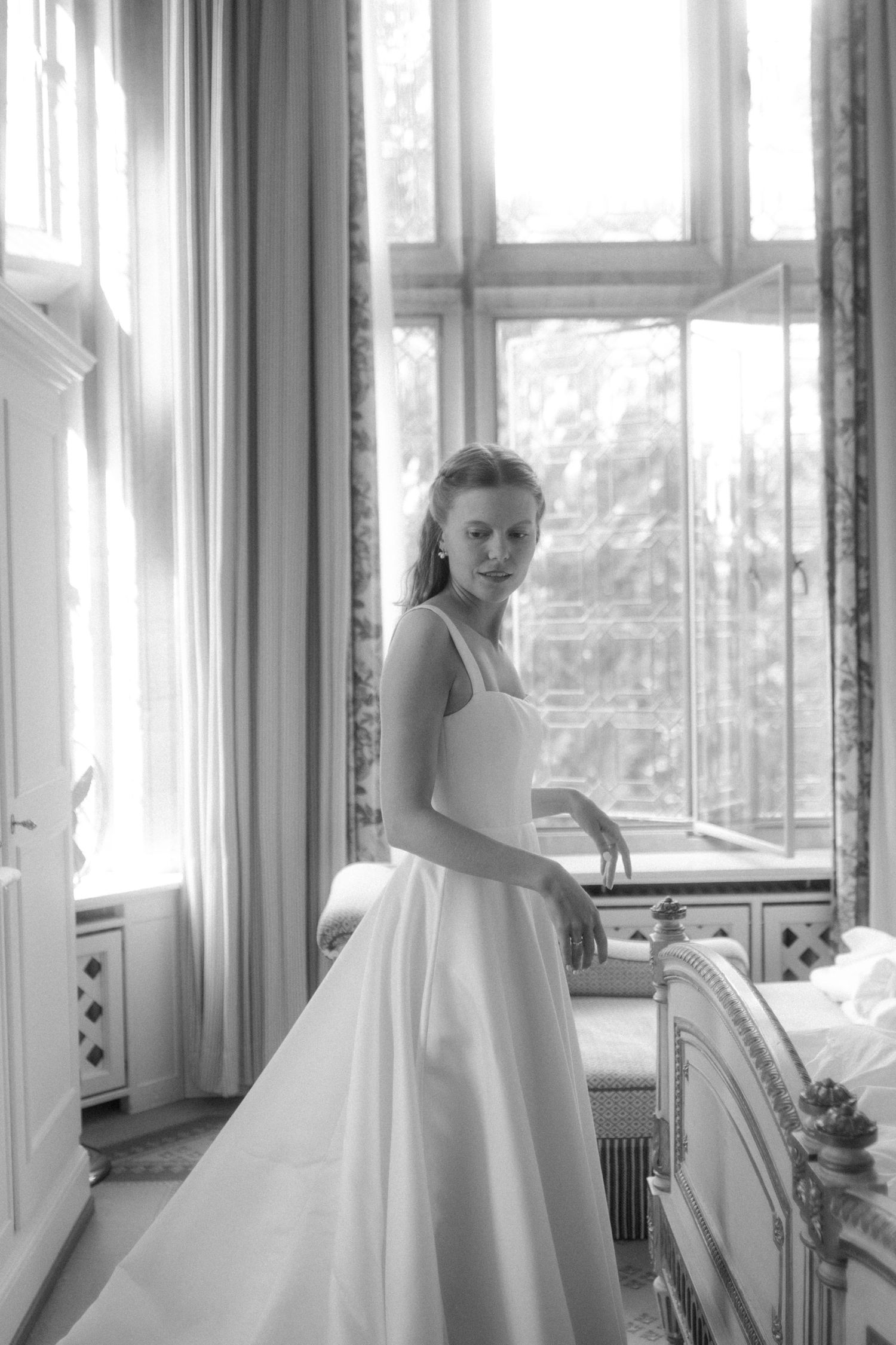 Figure in flowing white dress poses elegantly against bright windows in classic interior.