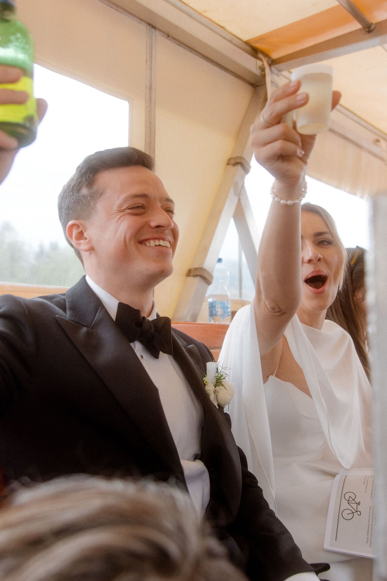 Joyful bride and groom raising glasses in a toast aboard a boat during their wedding celebration.