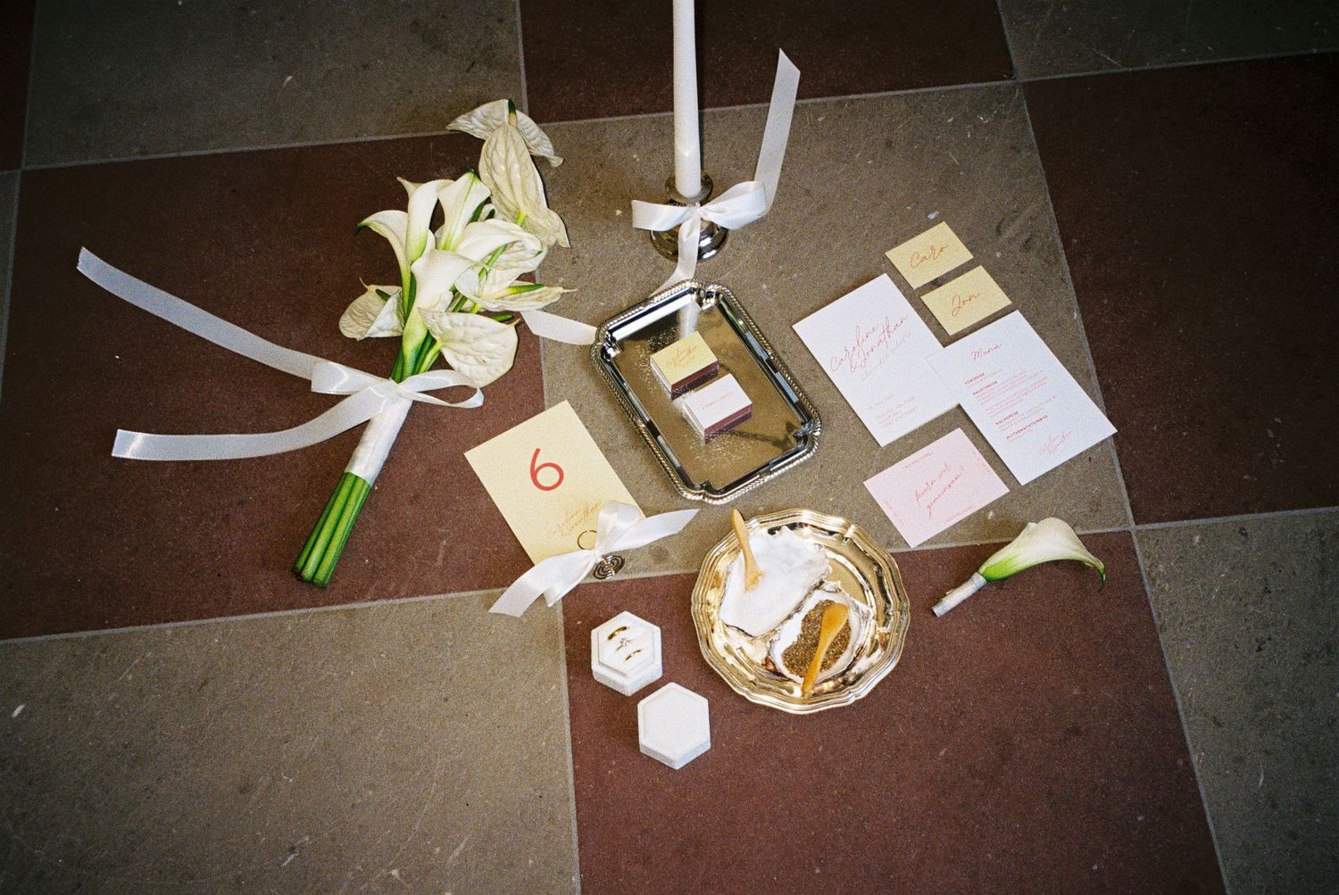 Wedding details including white lilies, ribbons, and small decorative items arranged on a dark tiled floor.