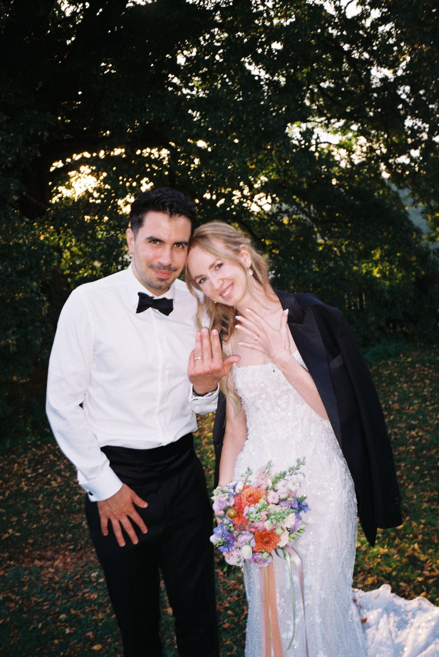 A couple in wedding attire share playful moments in an outdoor setting with trees and natural lighting.