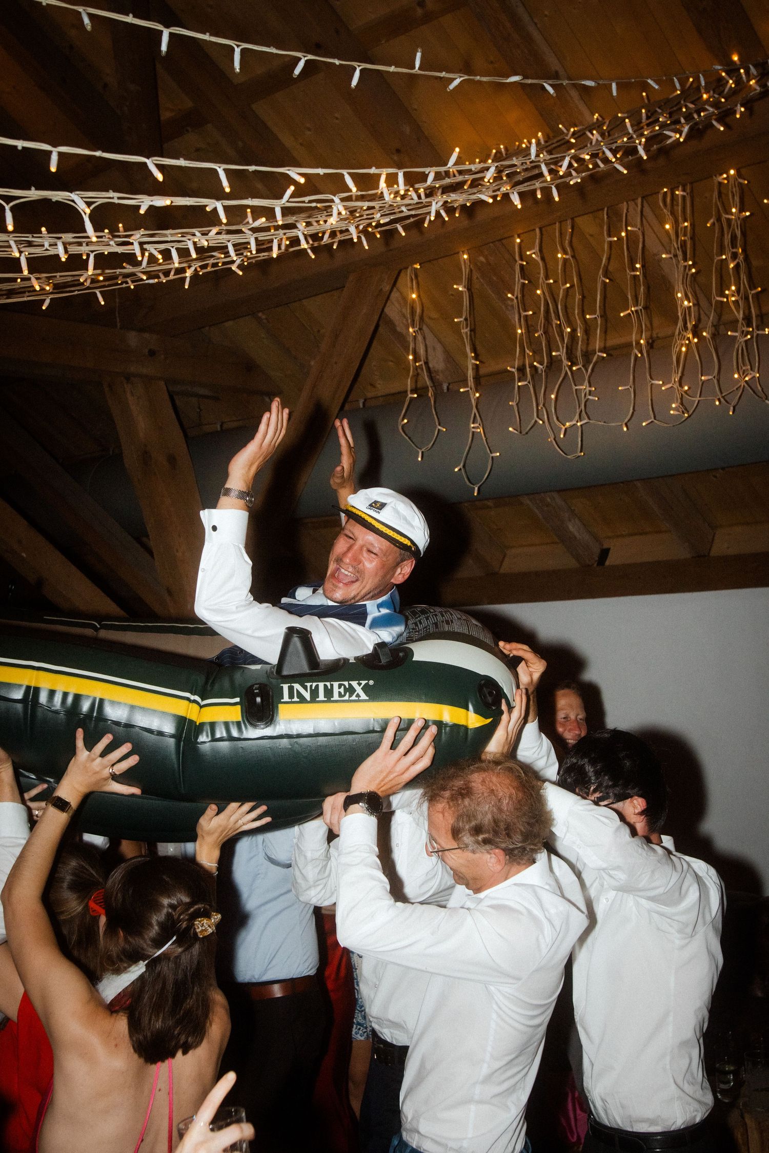 Celebratory scene with person being lifted on inflatable raft under decorative ceiling lights.