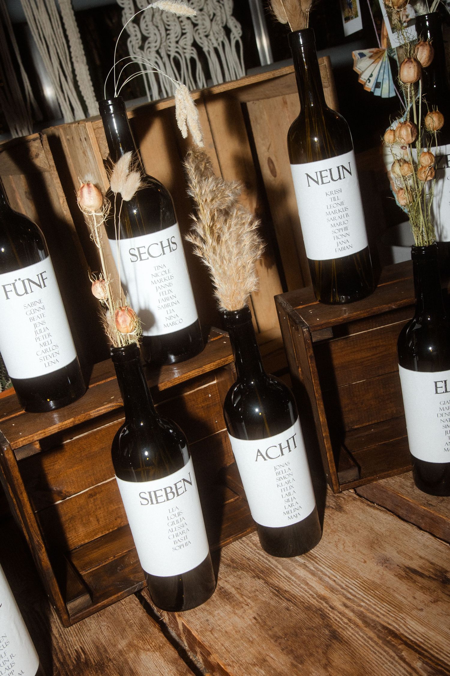 Wine bottles with minimalist labels displayed on wooden shelves with dried flowers and decorative elements.