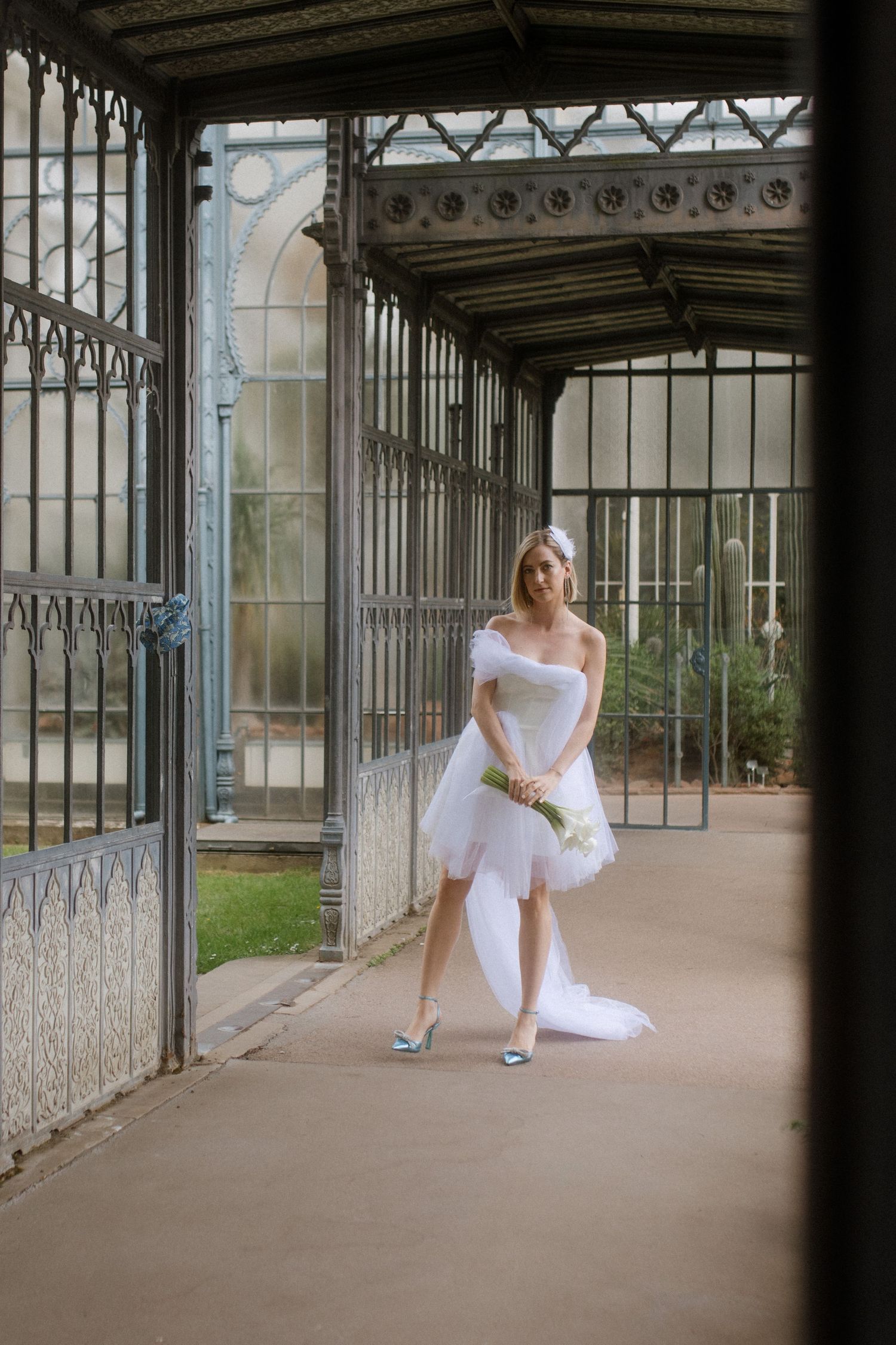 Person in a short wedding dress poses in an ornate covered walkway with architectural details.