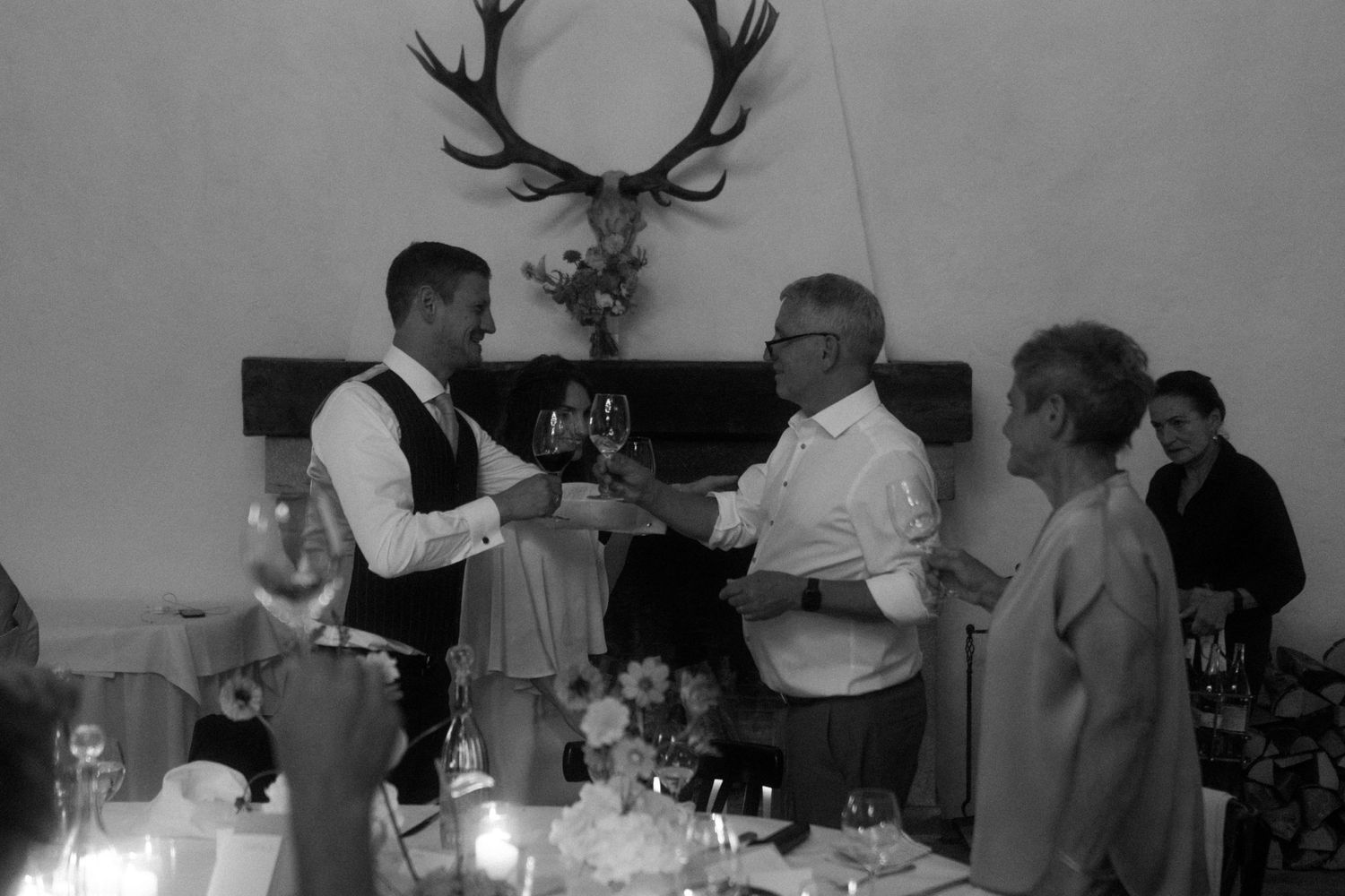 Vintage black and white photo of people gathered at a dinner with antlers mounted on wall.