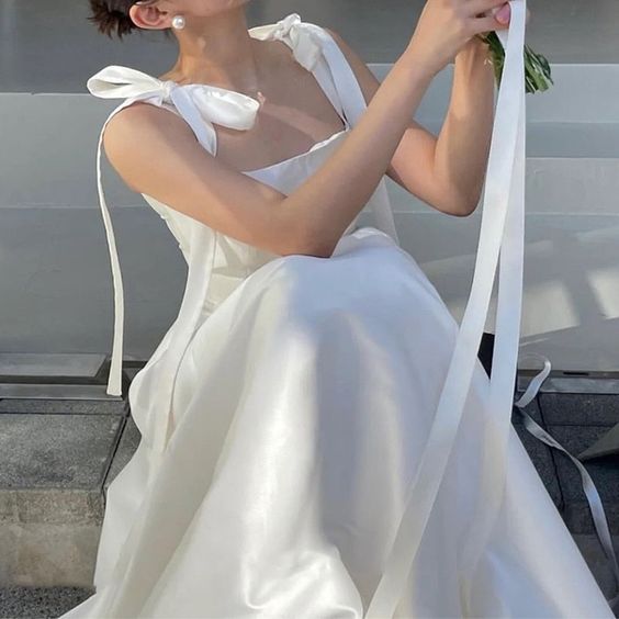 A white wedding dress with bow details shown from the waist up in natural light.