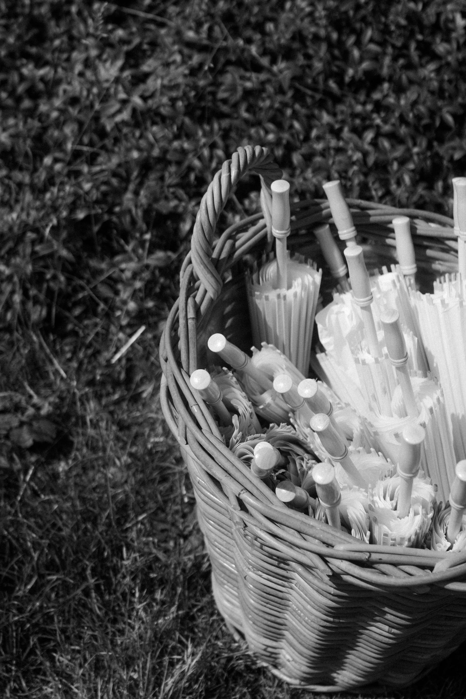 Black and white image of straws and utensils arranged in a woven basket.