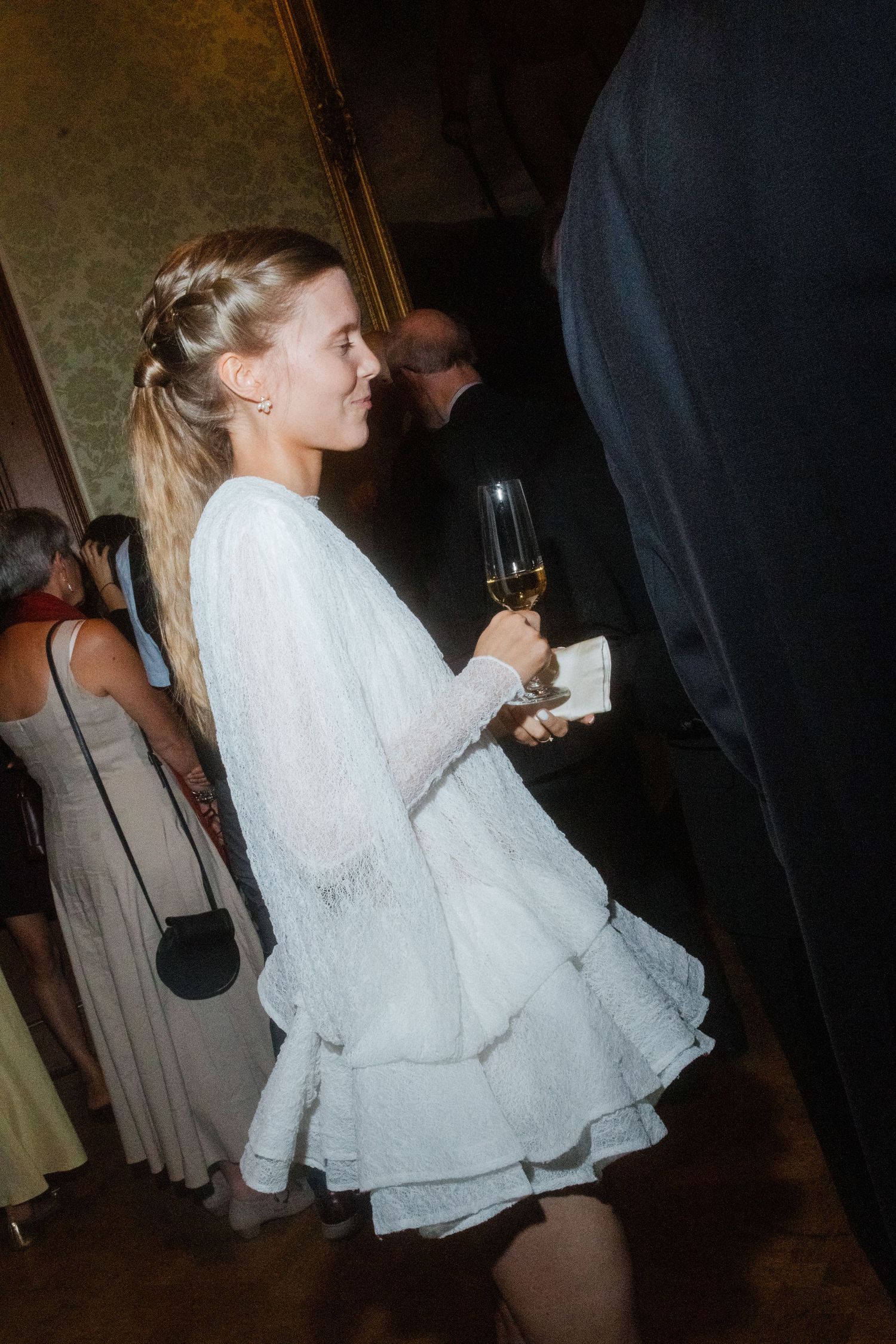Person in flowing white dress moving through dimly lit elegant room.