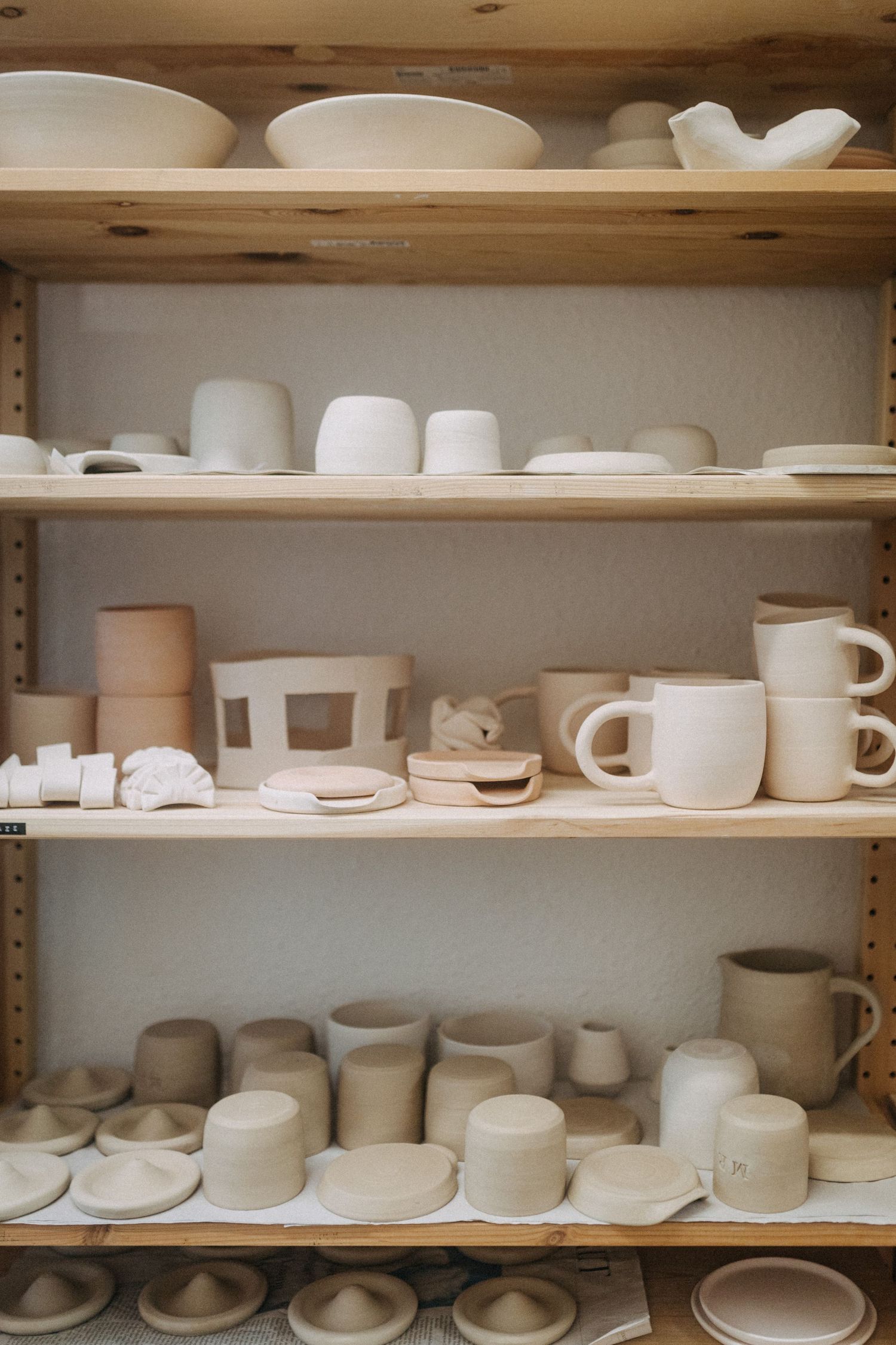 Wooden shelves displaying various white ceramic vessels and pottery pieces in a studio setting.