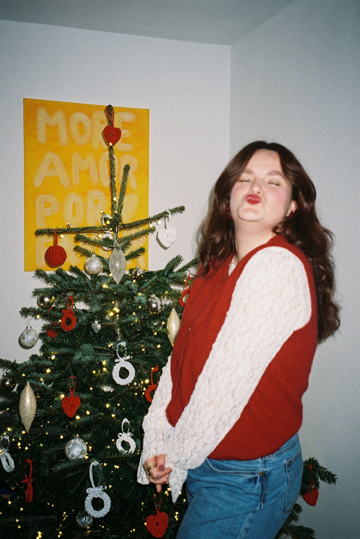 A series of four photos showing someone in a red sweater and jeans dancing playfully in front of a decorated Christmas tree.