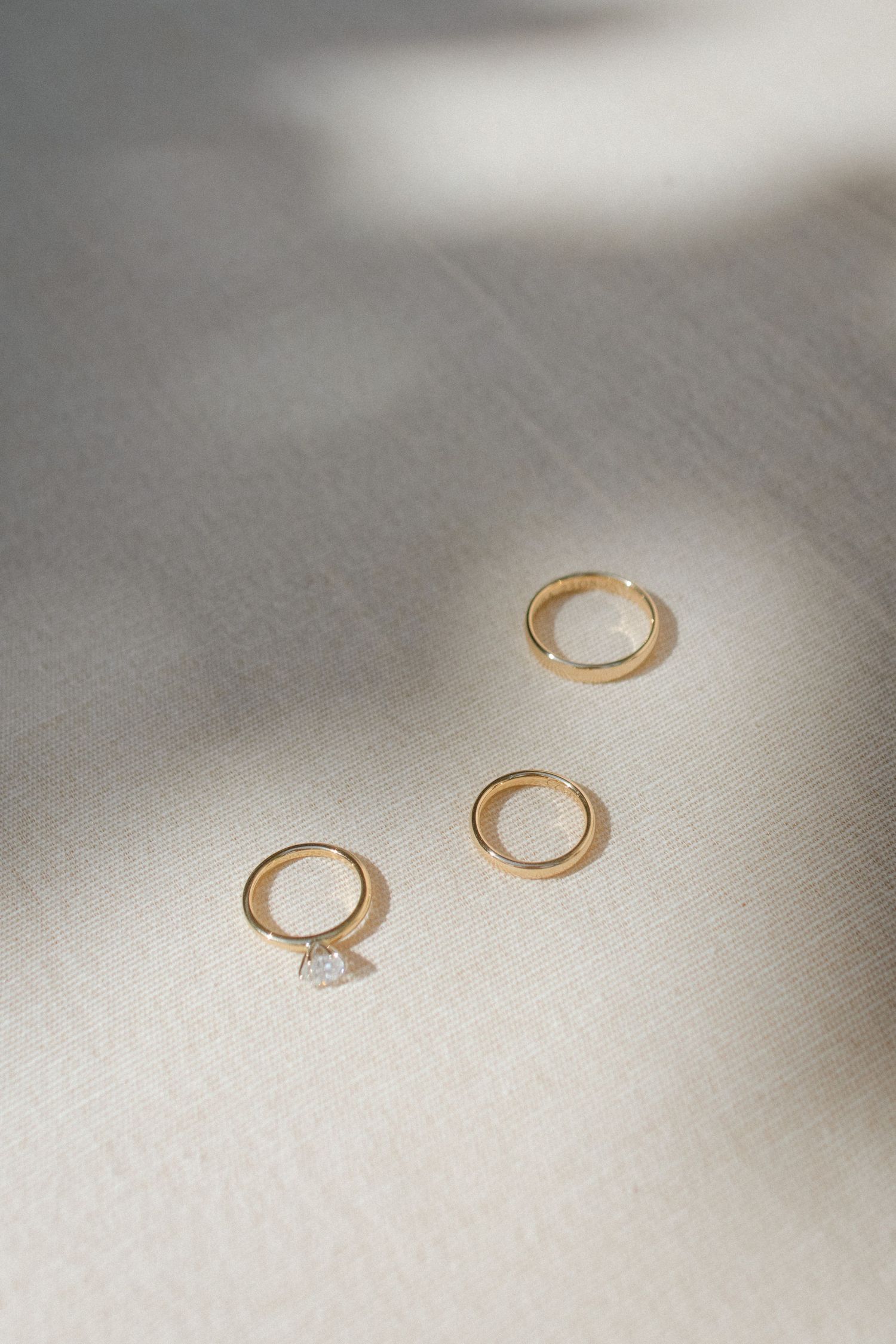 Gold wedding rings and engagement ring arranged on light gray surface with soft shadows.