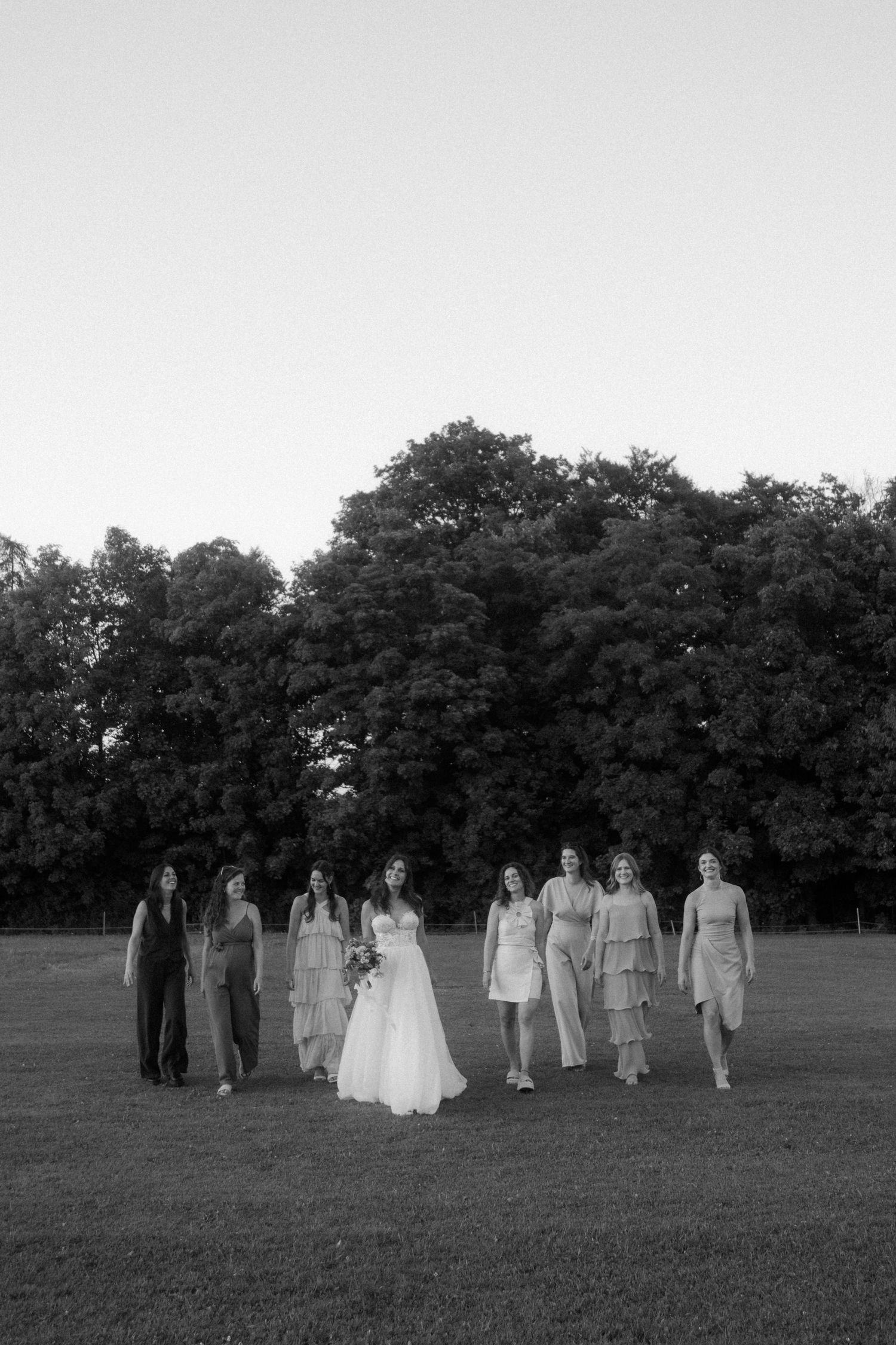 Wedding party walking across a grassy field at dusk.