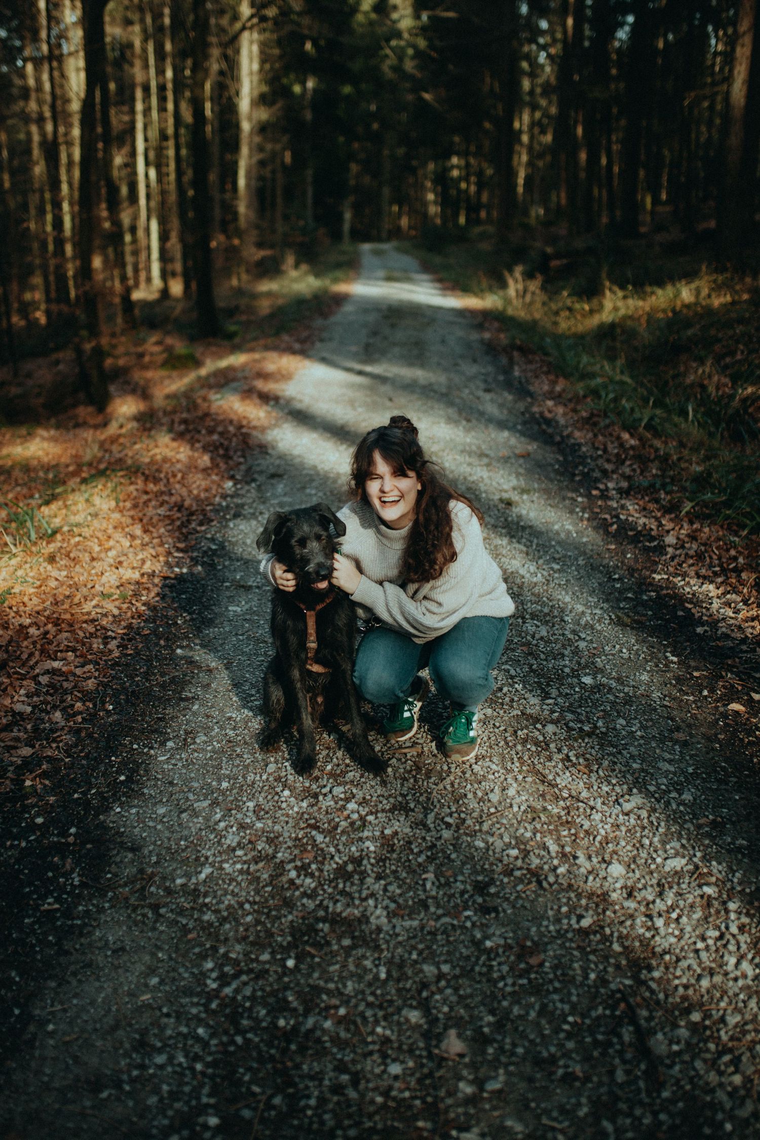 Person and black dog playing together on a forest path.