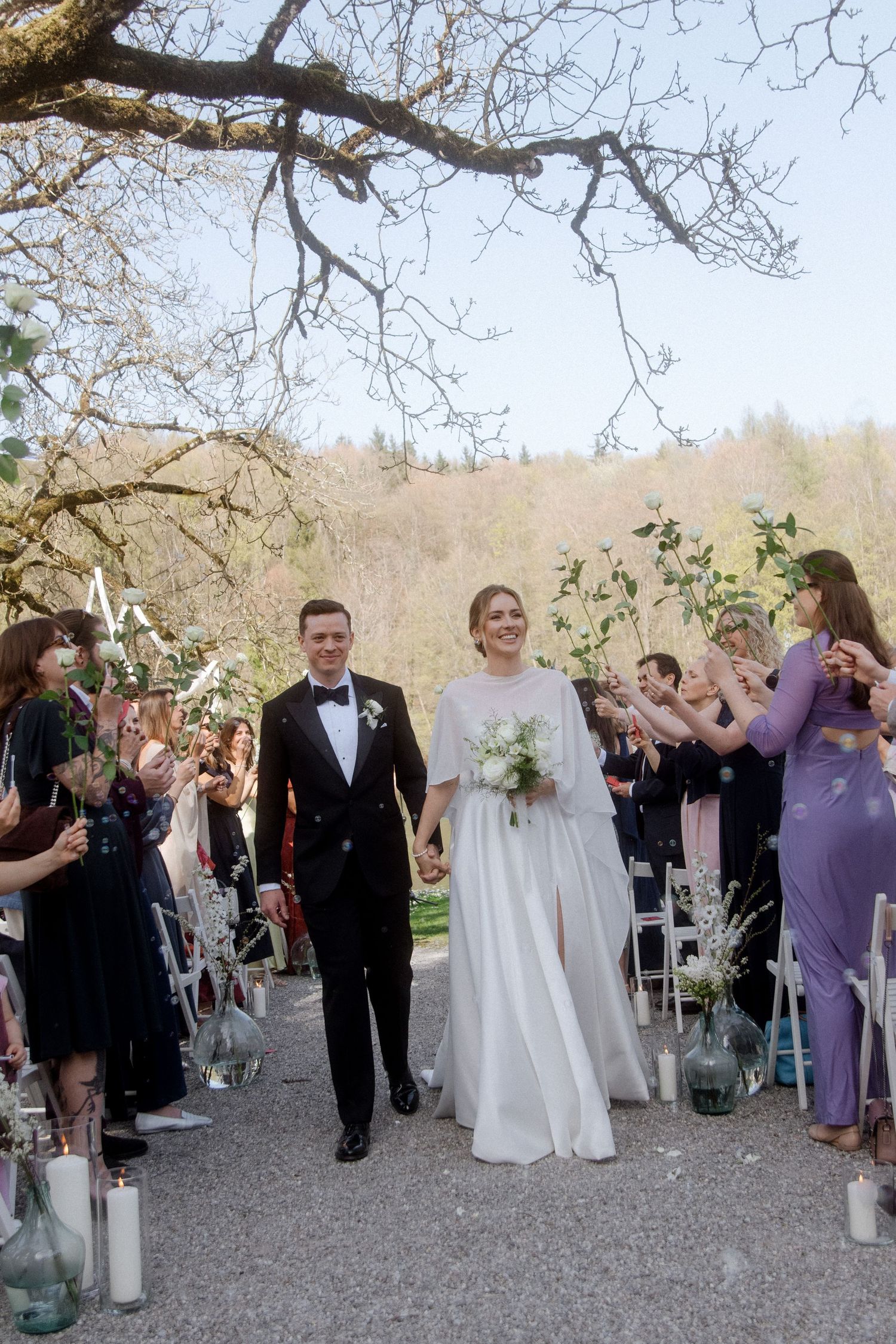 Happy newlyweds walk down outdoor aisle as guests celebrate their wedding ceremony.