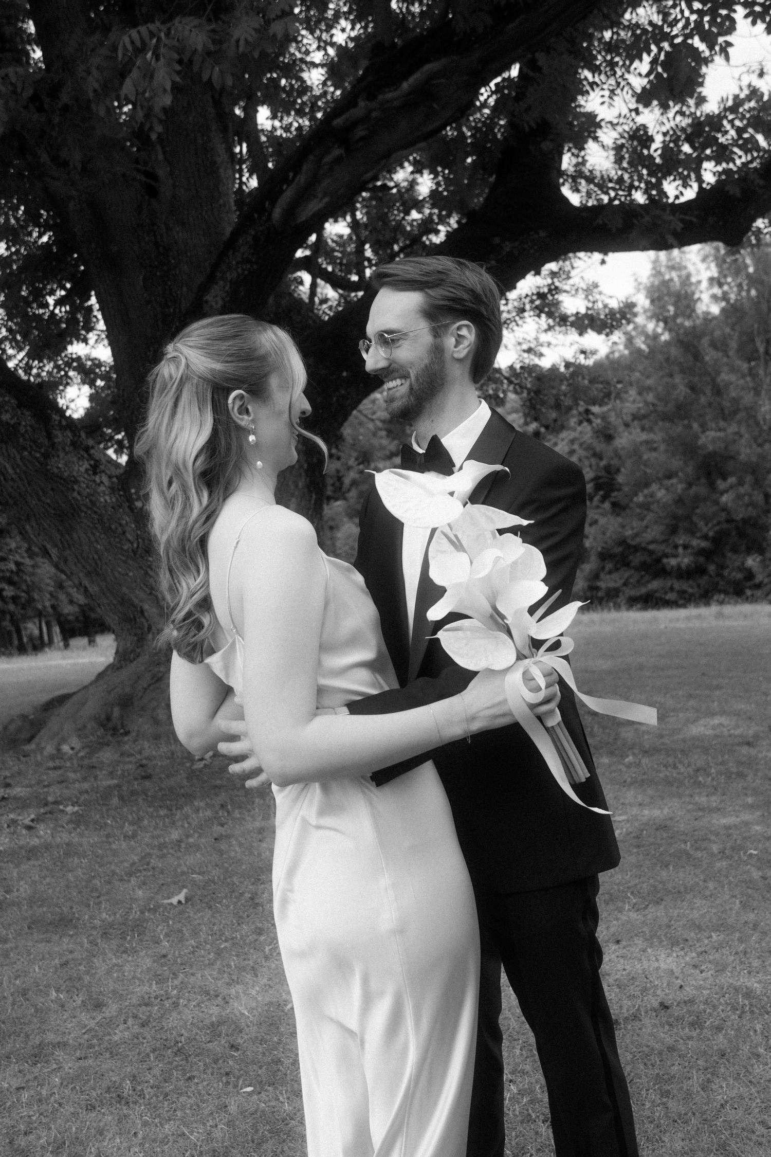 A romantic black and white portrait of a couple with white lilies under a tree.