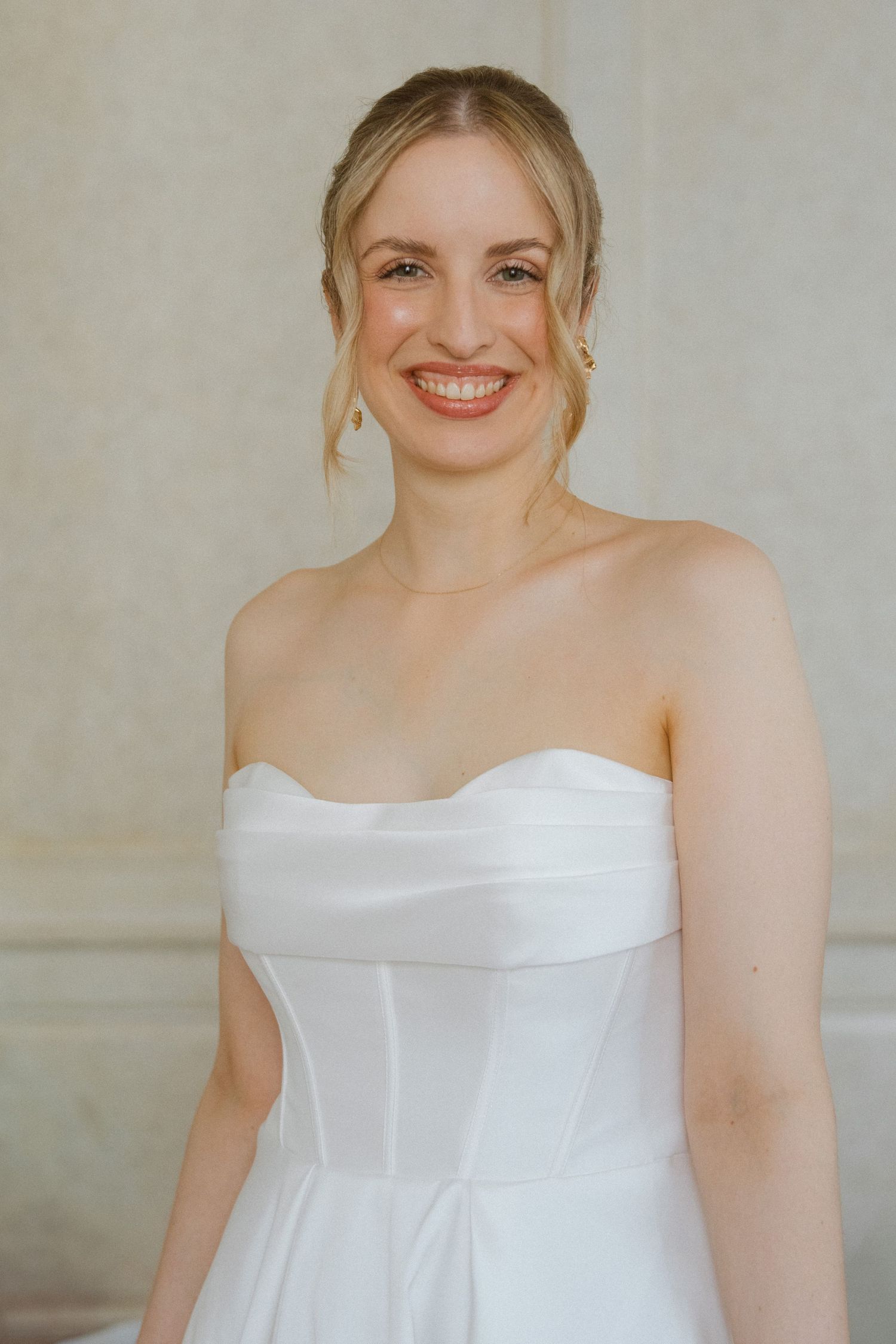 A bride wearing a strapless white wedding dress smiles warmly.
