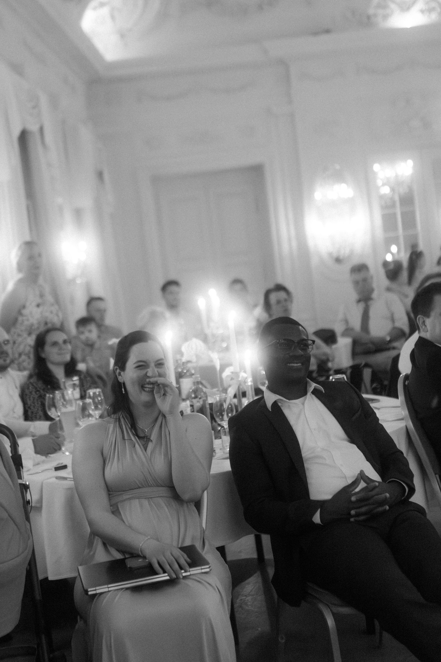 Wedding reception guests seated in an elegant white ballroom with crystal chandeliers.