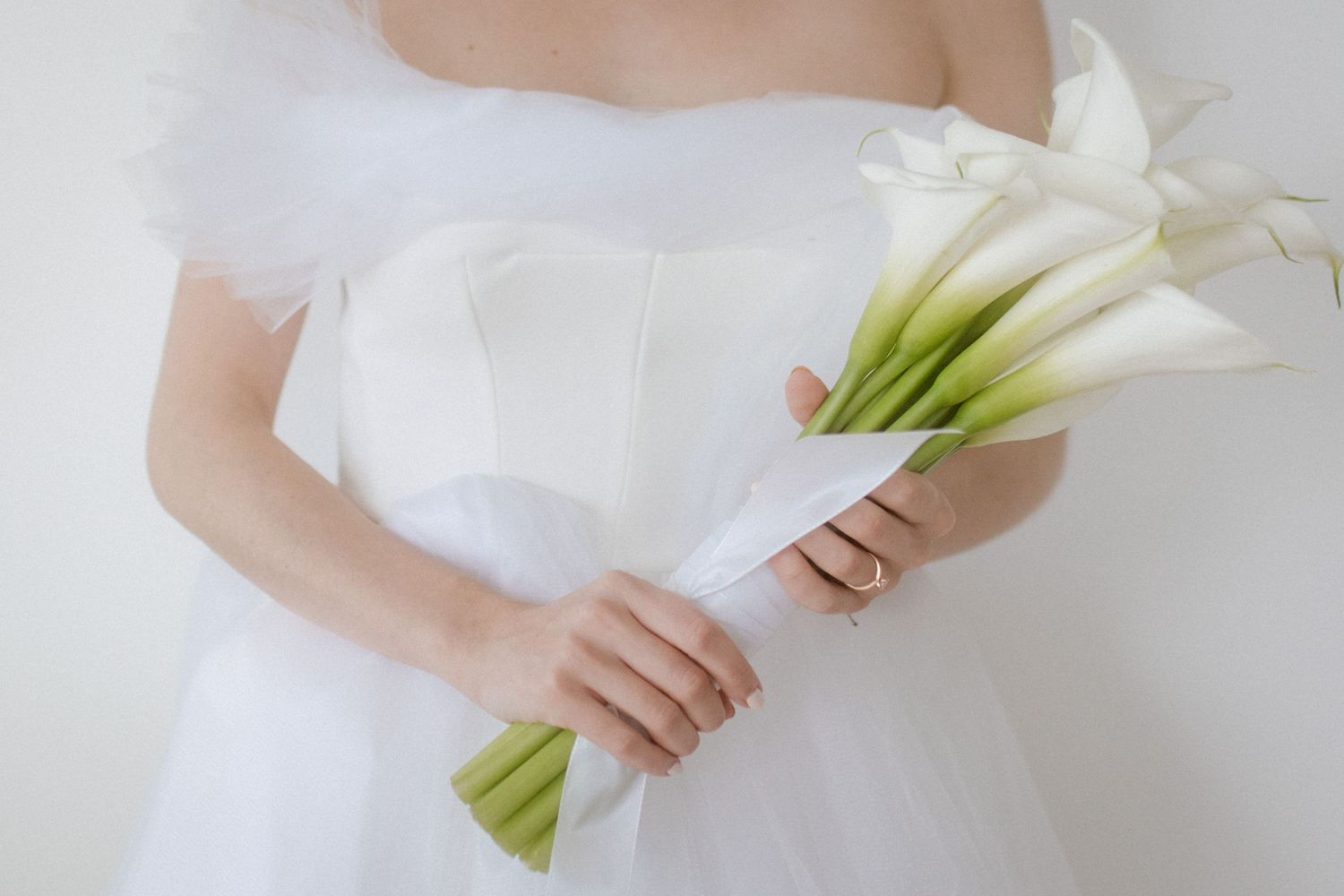 Close up of white calla lily bouquet held against white wedding dress.