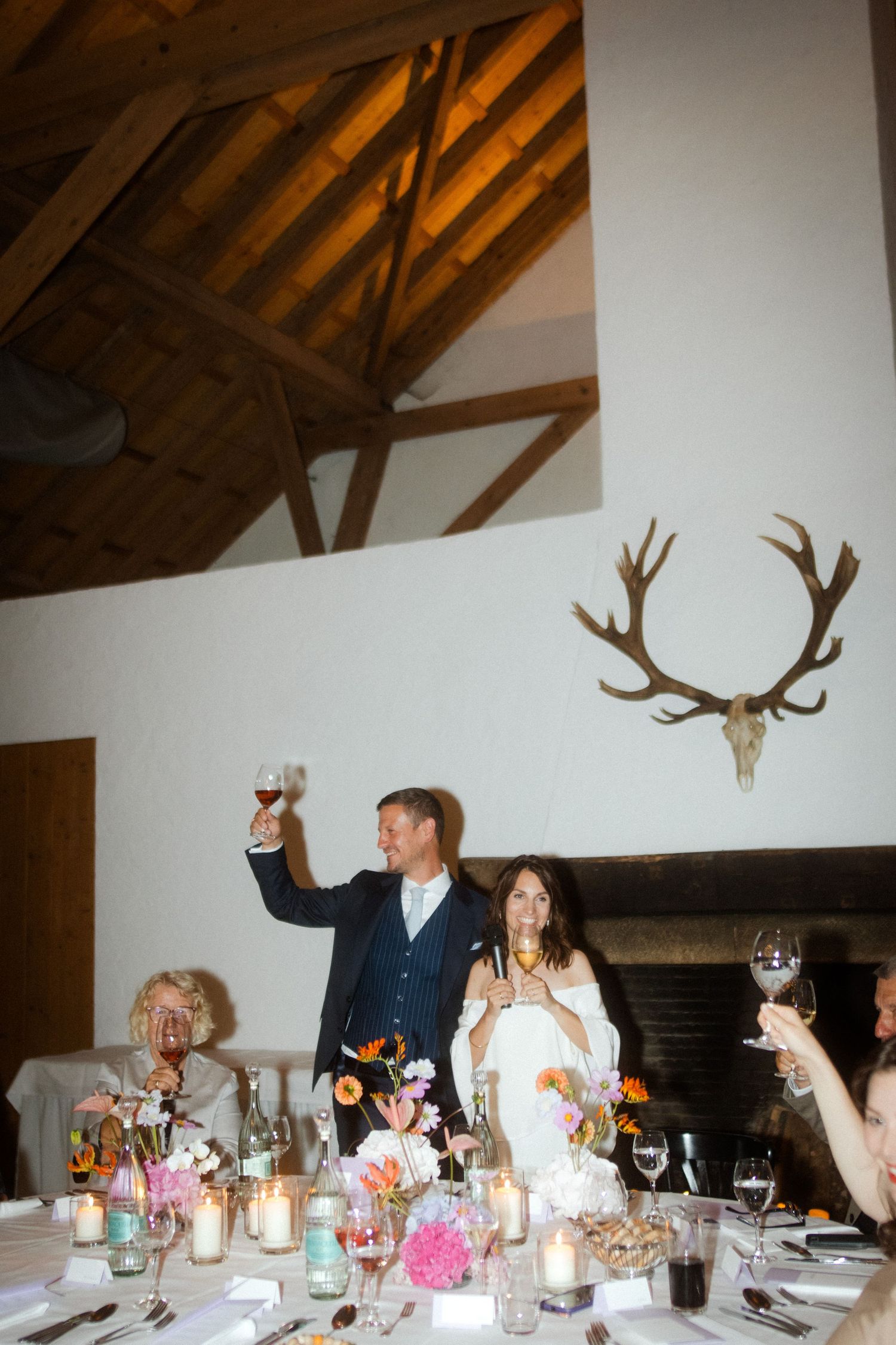 Wedding celebration moment with rustic decor and antler mount on white wall.