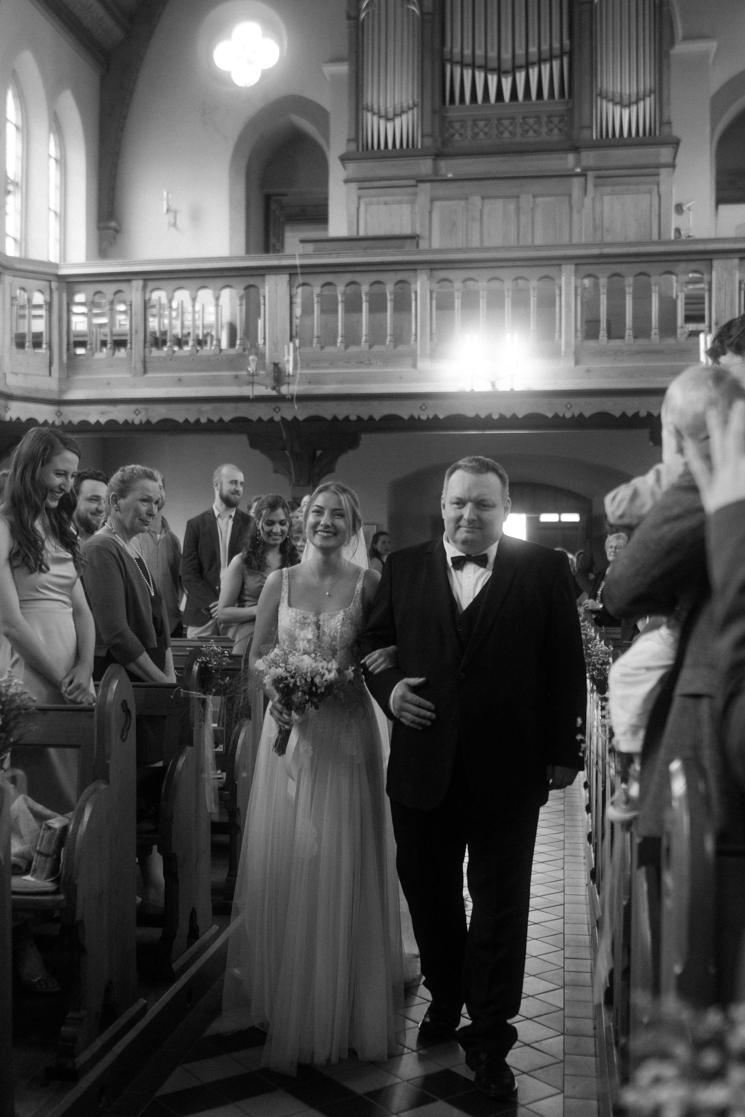 A church wedding ceremony processional takes place in a traditional sanctuary with wooden pews.