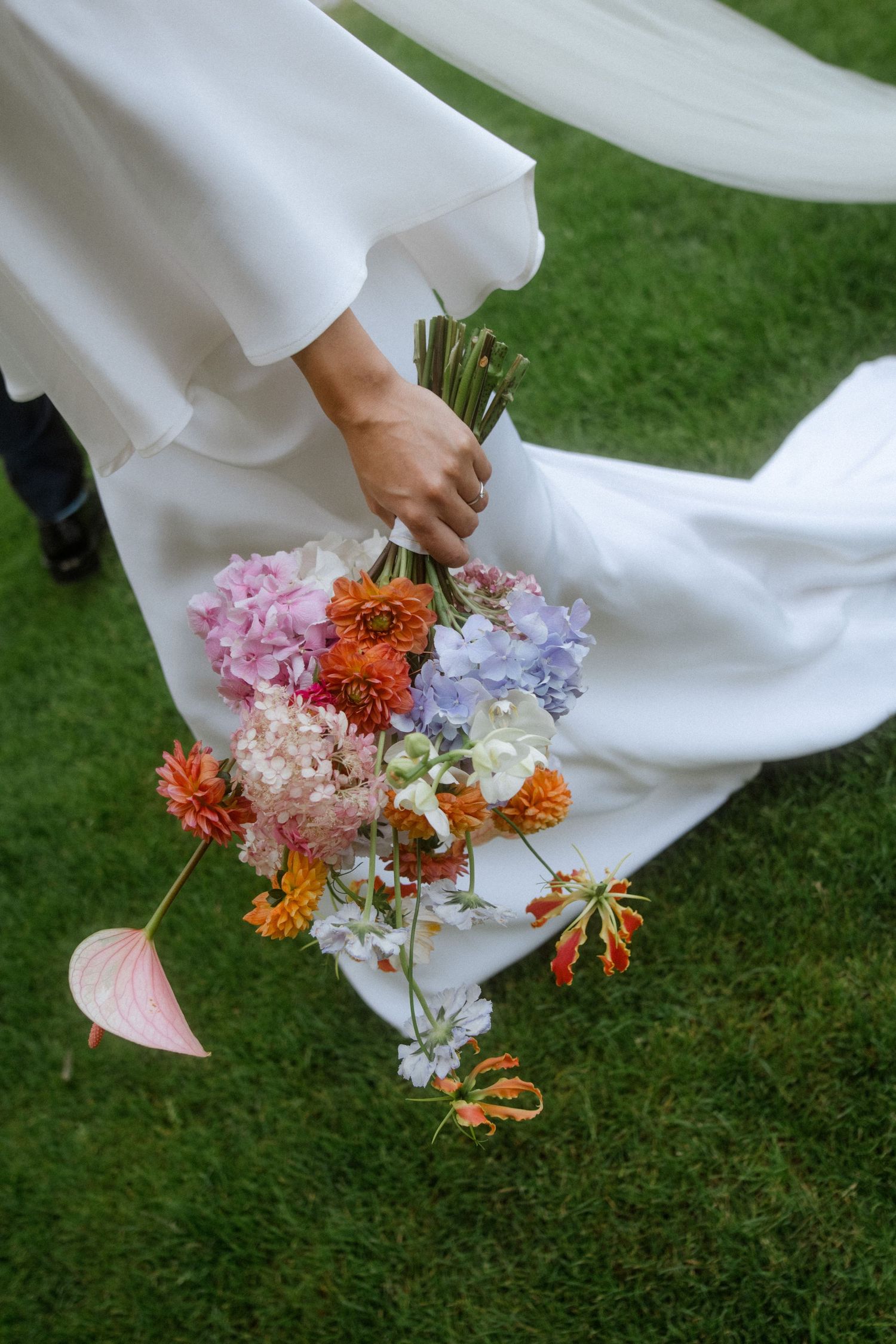 Colorful wildflower bouquet with pink and orange blooms against flowing white wedding dress.