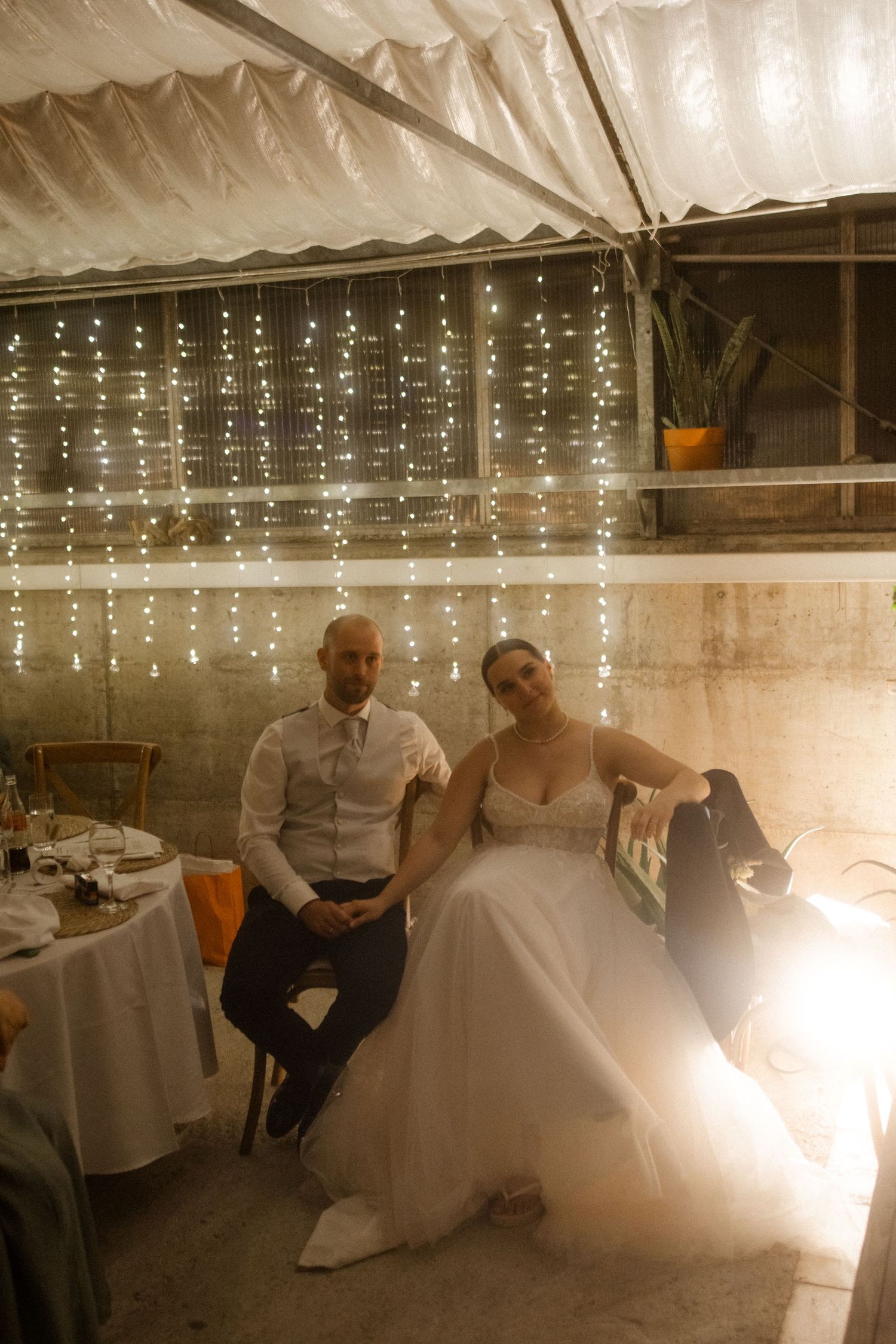 Couple resting at wedding reception under romantic fairy light backdrop.
