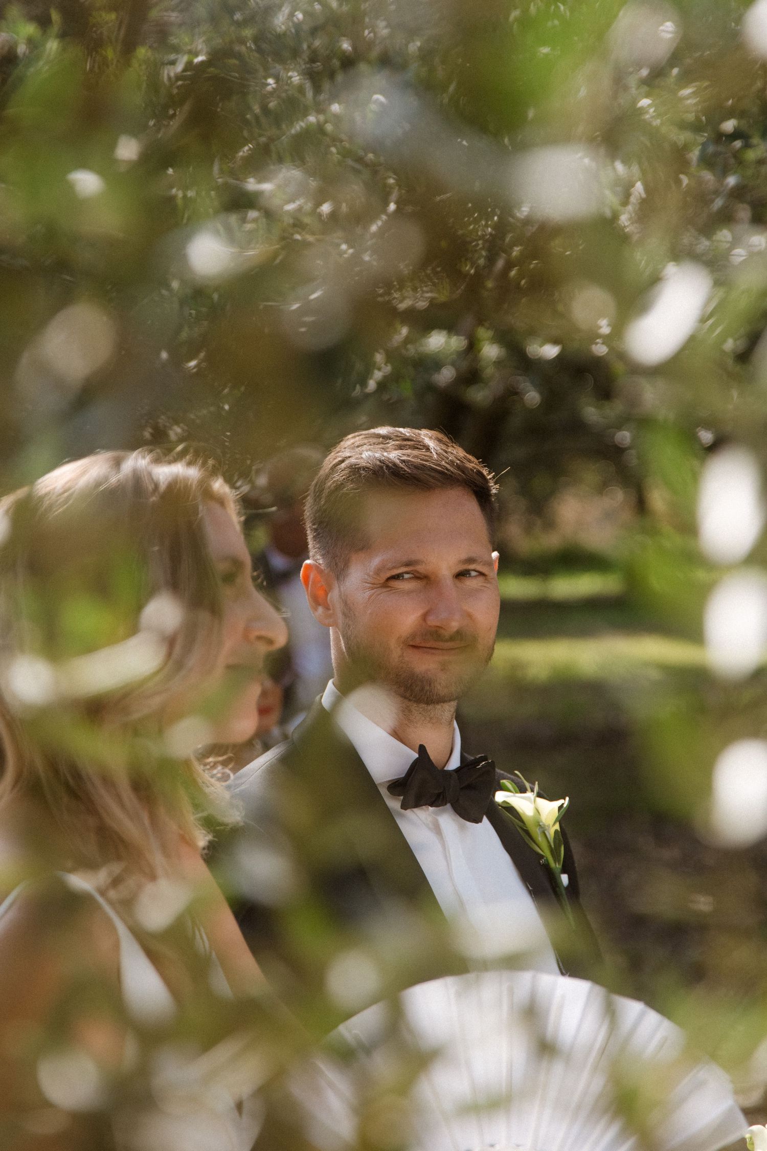 Elegant outdoor wedding portrait through bokeh leaves and sunlight.