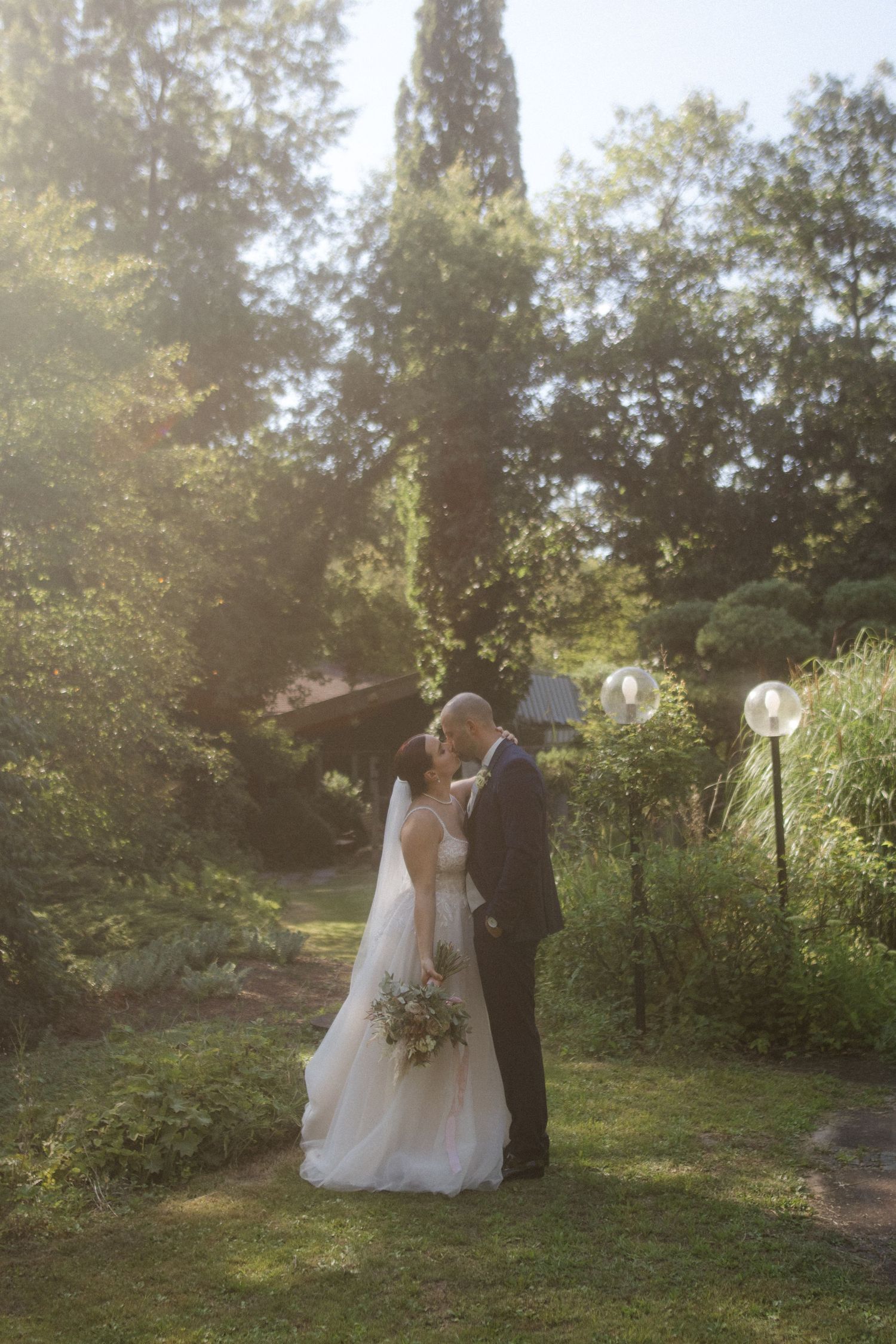 Romantic sunset wedding portrait in garden setting with glowing string lights.