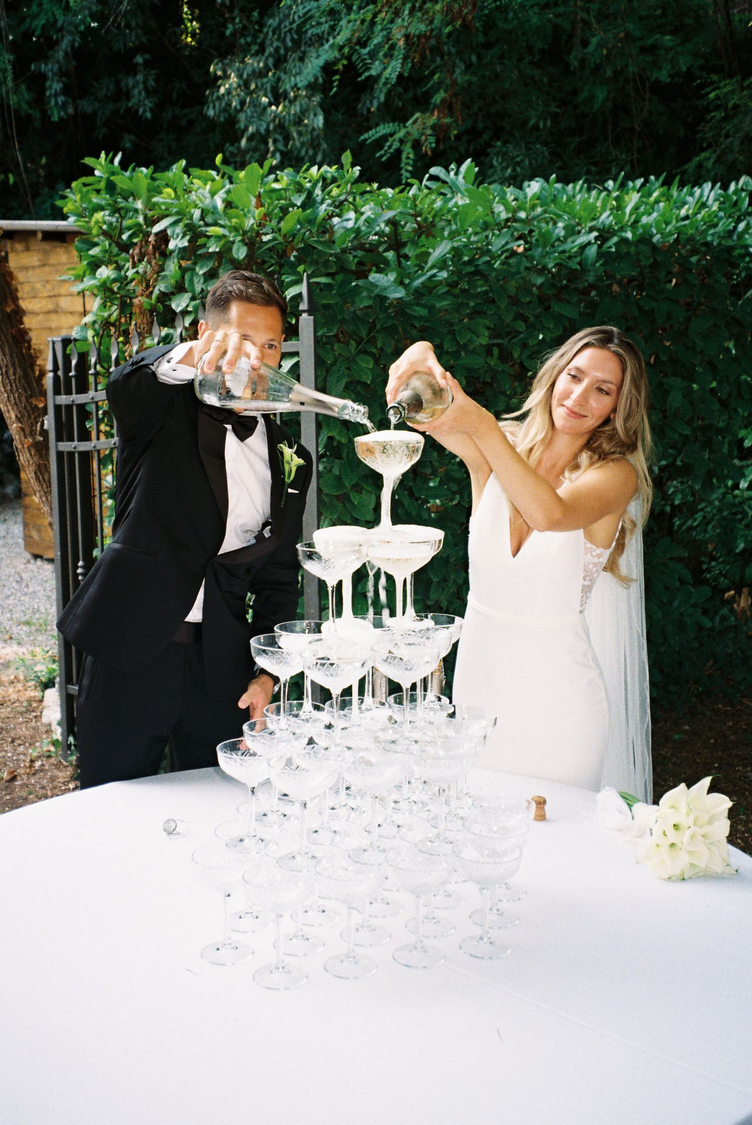 Elegant champagne tower being built at an outdoor wedding reception.