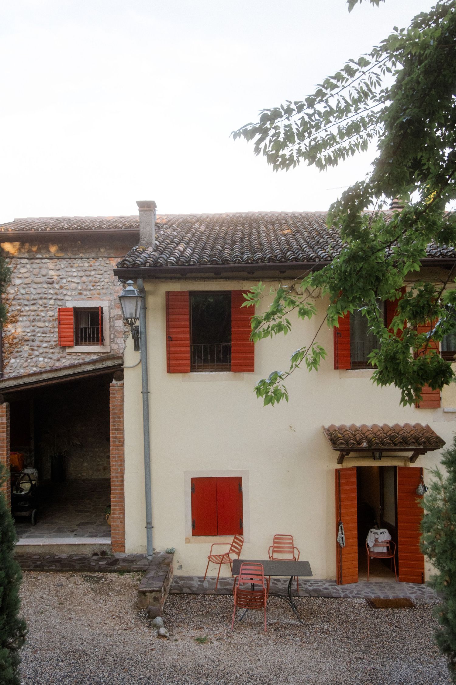 Italian villa with red shutters and stone walls featuring outdoor seating area.