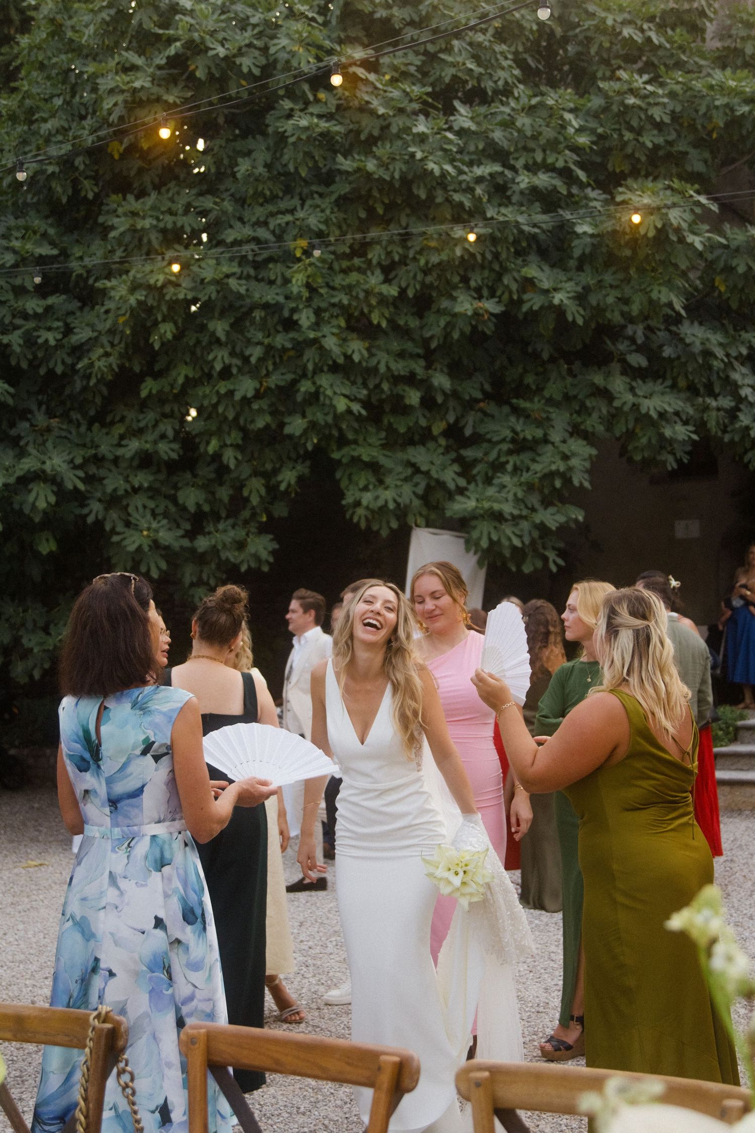 Wedding guests mingle and celebrate at an outdoor reception under string lights and trees.